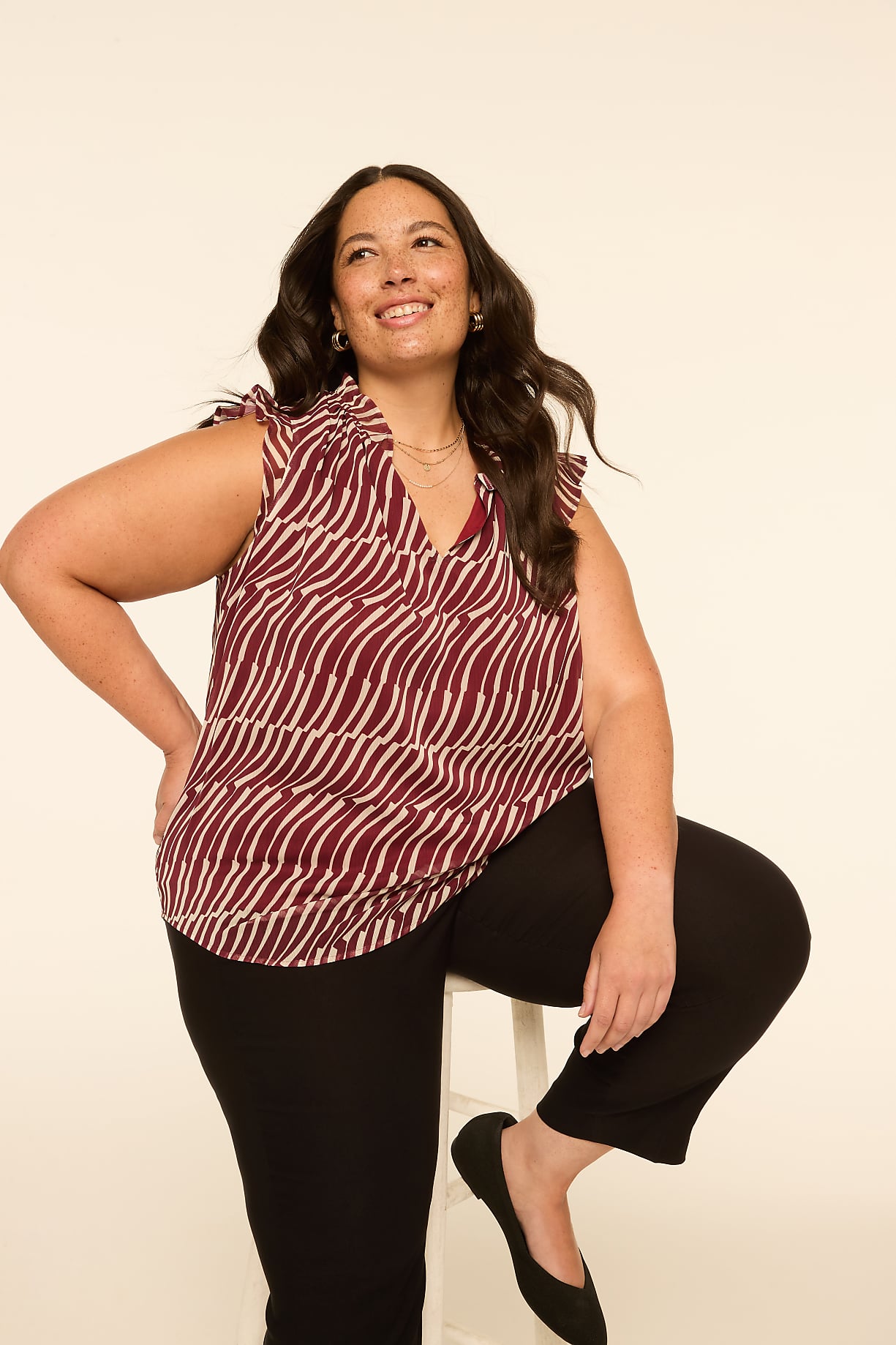 A woman in a patterned top and black pants poses against a plain, light-colored background. Product Image 7