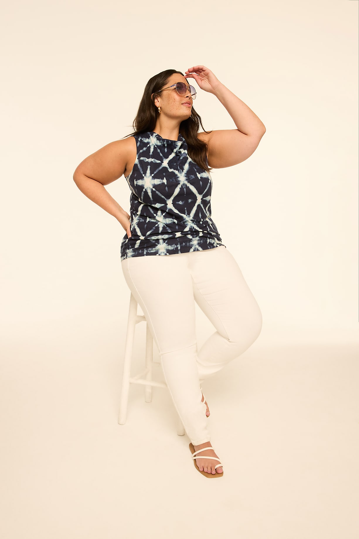 A woman in a tie-dye top and white pants sits on a stool against a plain, light-colored background. Product Image 6