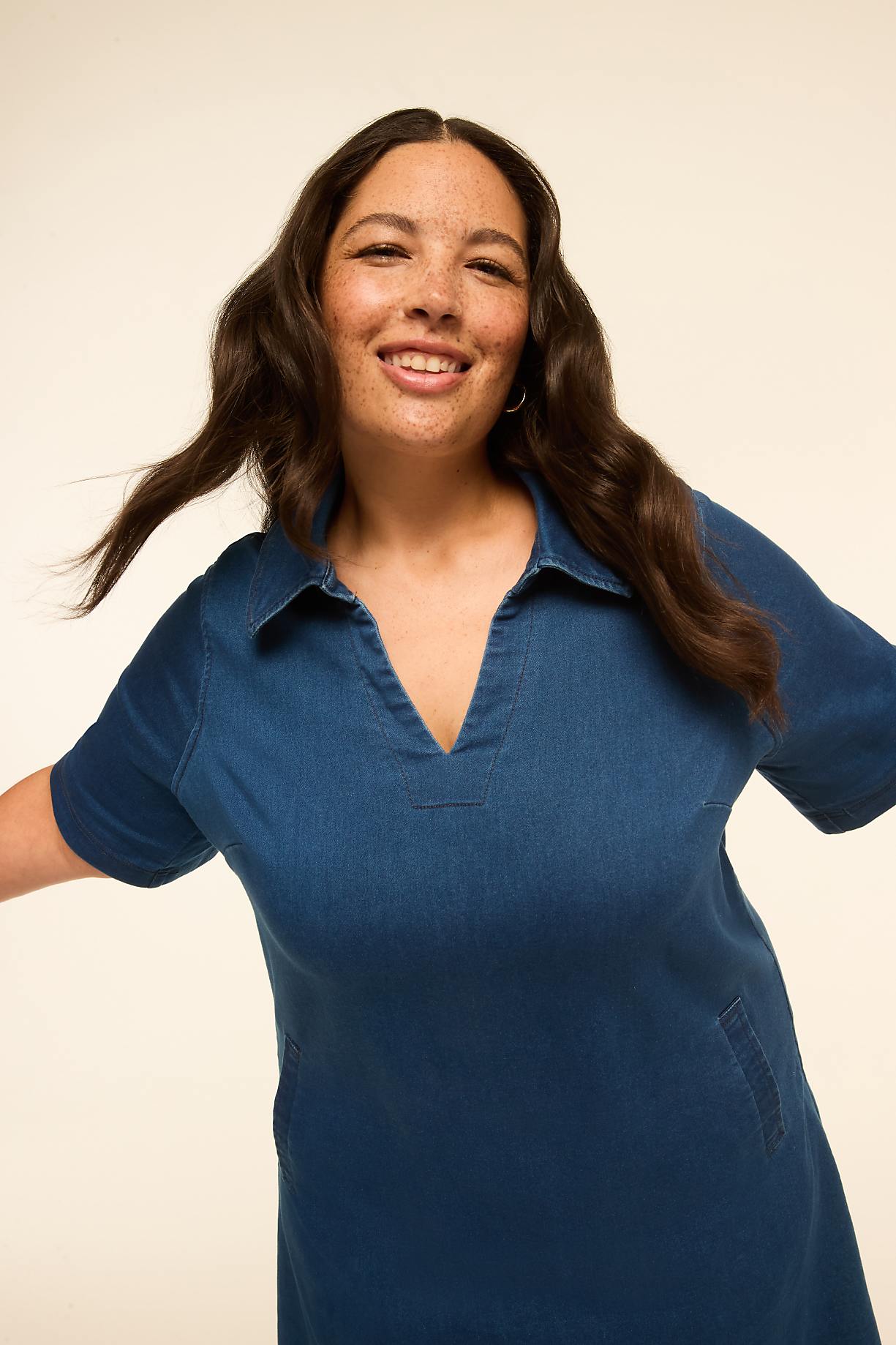 A smiling woman with dark, wavy hair and freckles, wearing a blue denim dress, is captured against a plain, light-colored background. Product Image 7