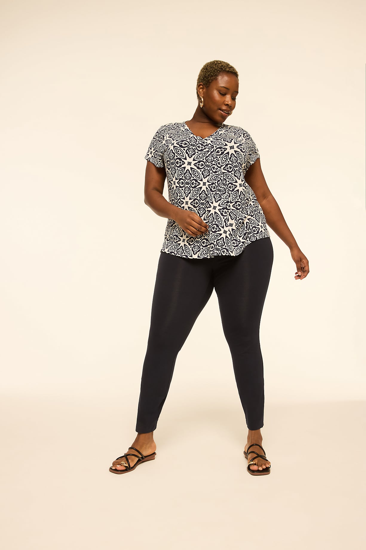 A woman in a patterned top and dark leggings stands against a plain, light-colored background. Product Image 6