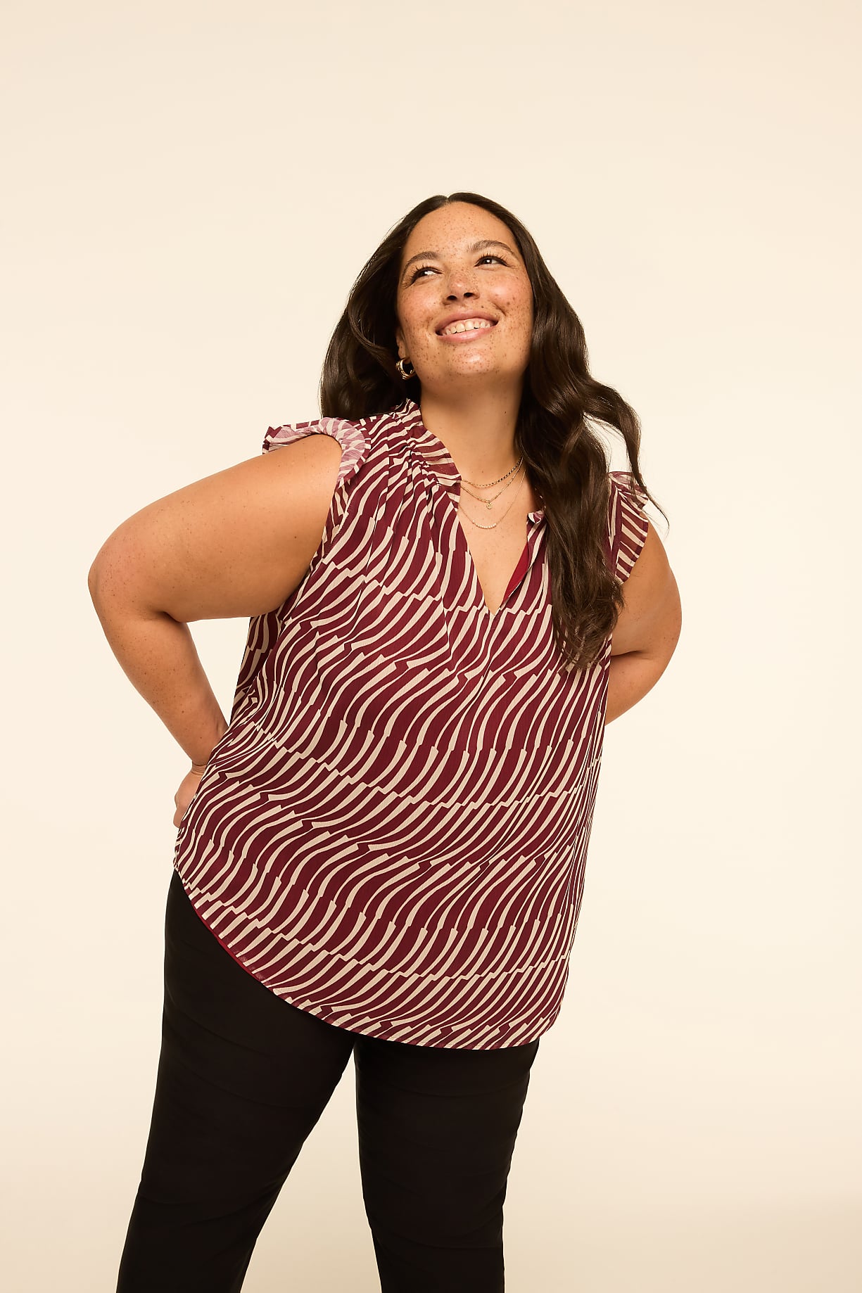A woman in a patterned top and black pants poses with her hands on her hips against a plain, light-colored background. Product Image 8