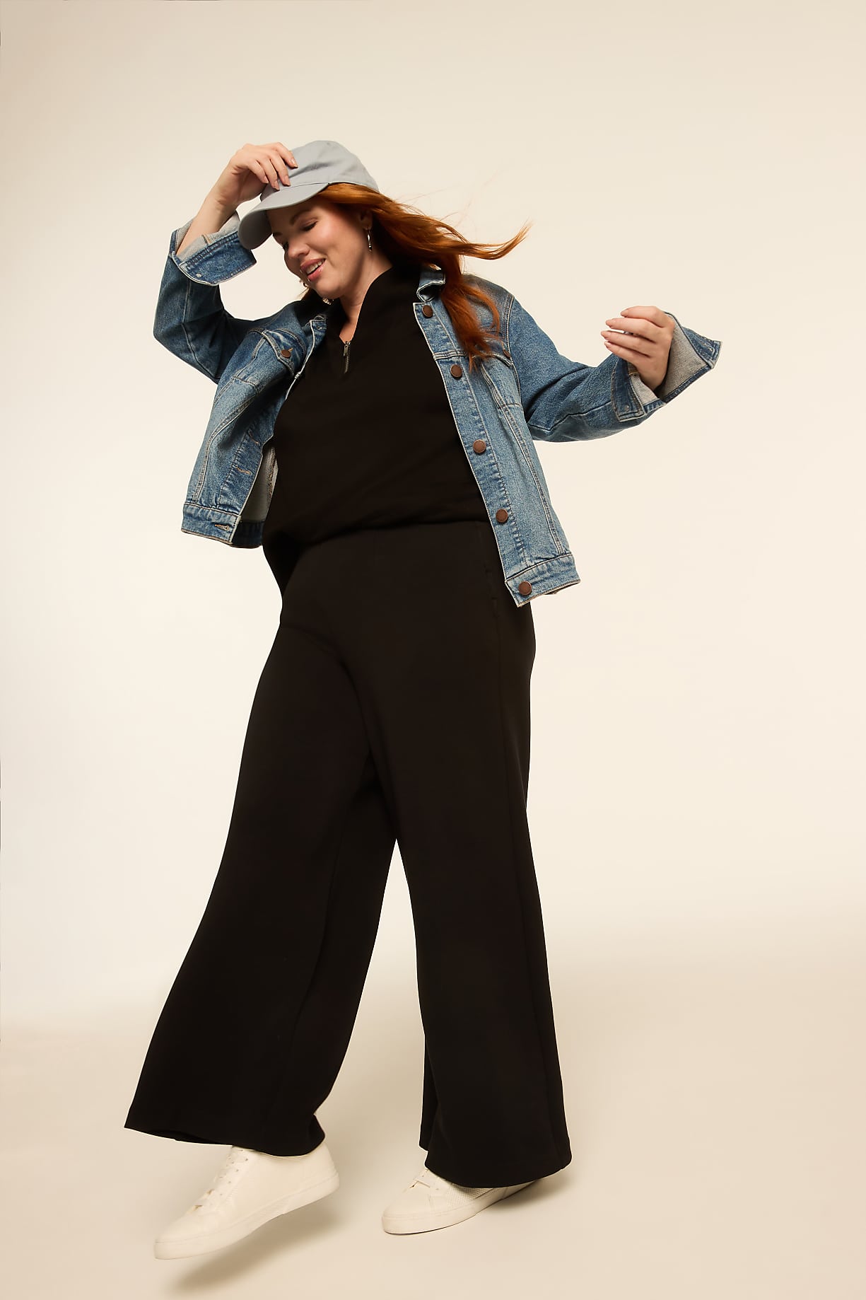 A woman with red hair in a denim jacket and black pants dances against a plain, light-colored background. Product Image 7