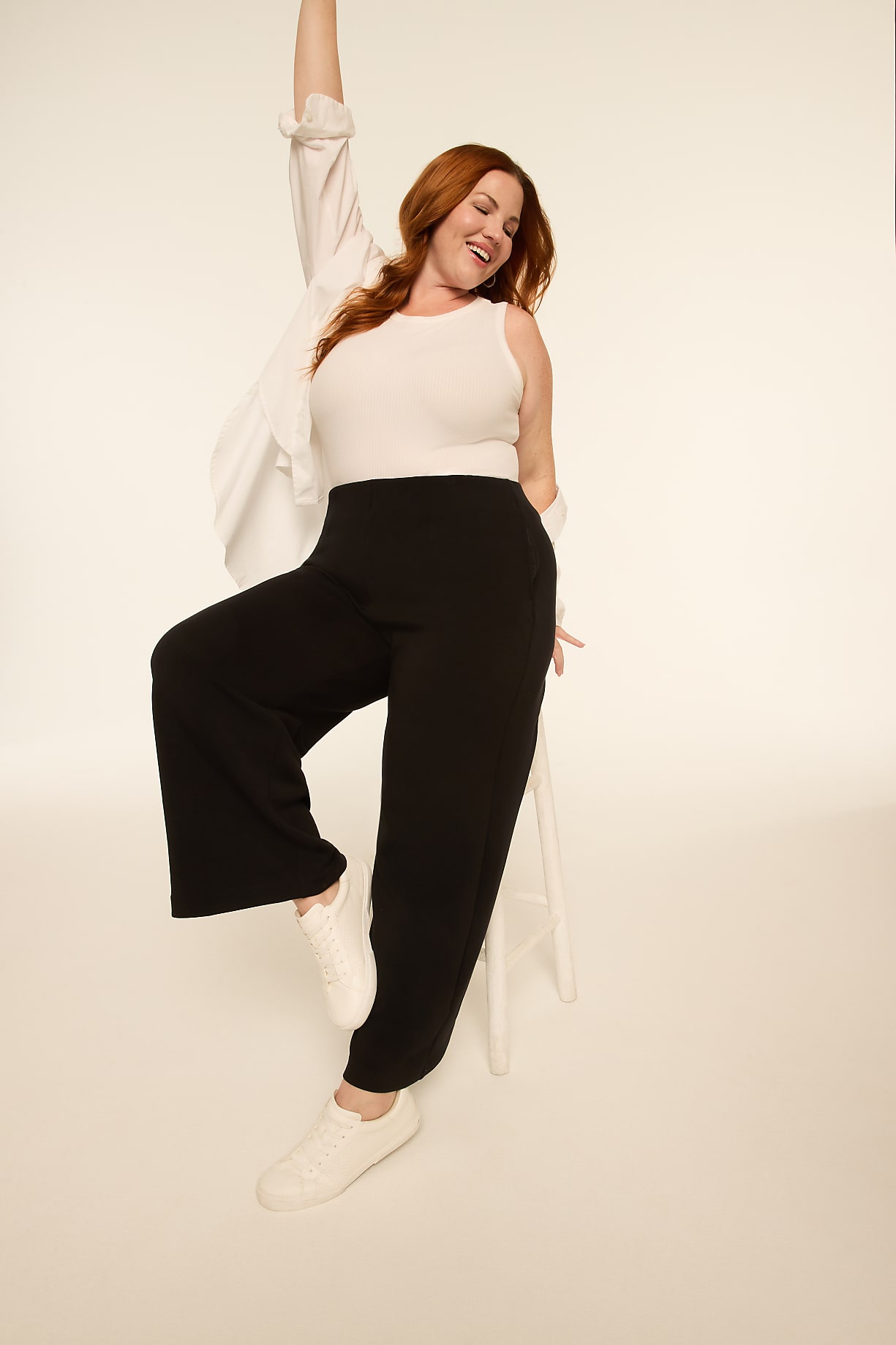 A woman with red hair in a white tank top and black wide-leg pants poses dynamically against a plain, light-colored background. Product Image 10