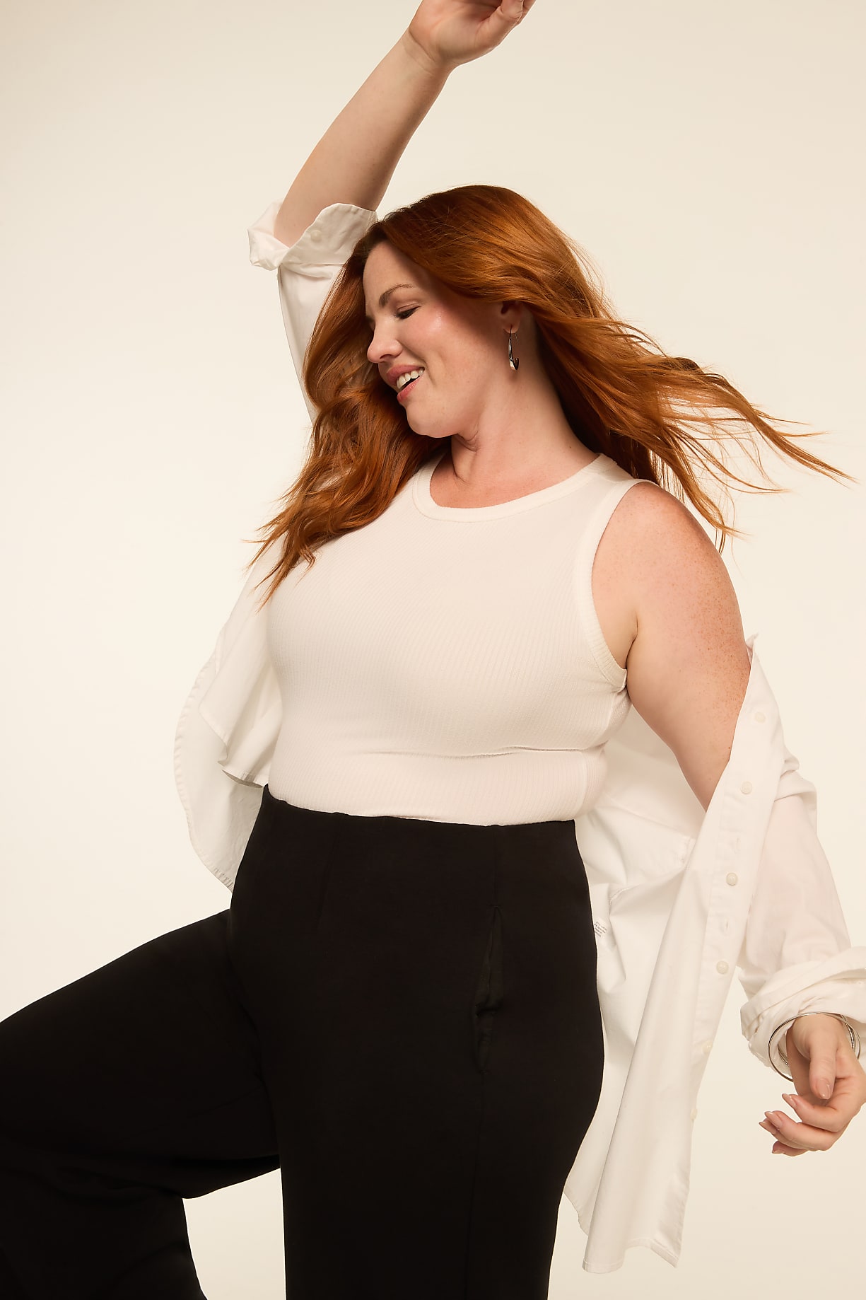 A woman with red hair in a white tank top and black pants dances against a plain, light background. Product Image 11