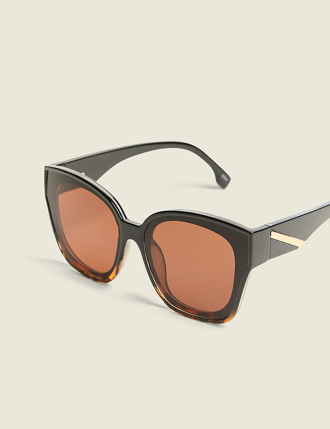 A pair of oversized, dark-rimmed sunglasses with amber lenses rests against a plain, light-colored background. Product Image 1