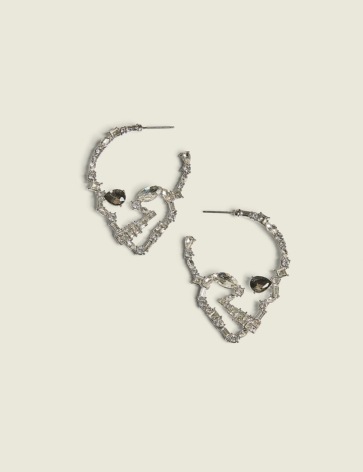 A pair of silver hoop earrings shaped like skulls with dark gem eyes rest on a pale yellow background. Product Image 1