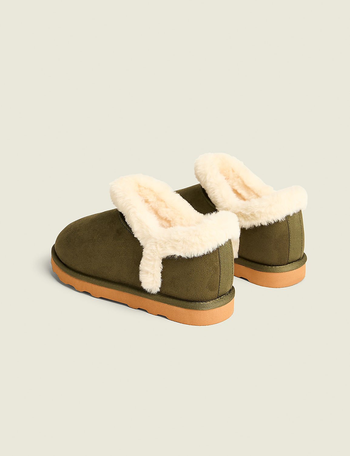 A pair of olive green, fuzzy-lined slippers with tan soles rests on a plain, light beige background. Product Image 2