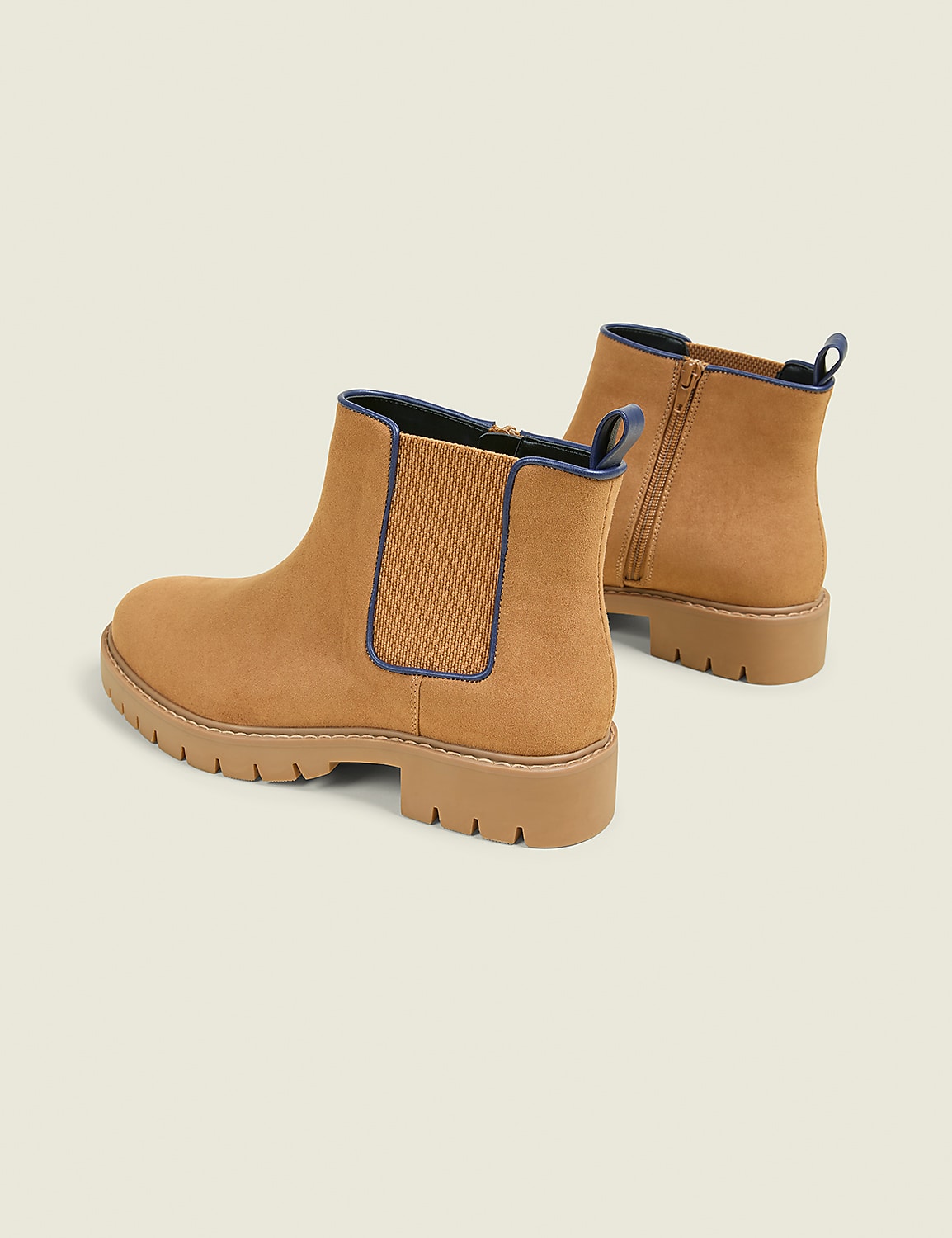 A pair of tan suede Chelsea boots with dark blue trim and lug soles are displayed against a plain, light beige background. Product Image 2