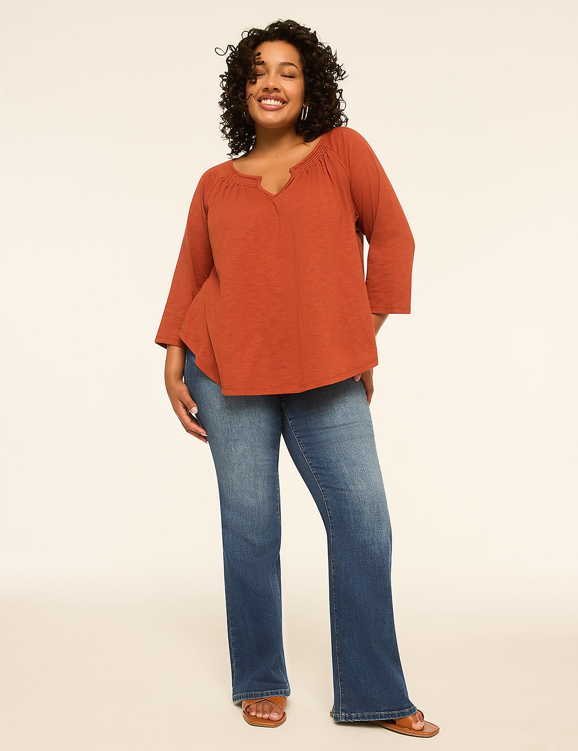 A smiling woman in a rust-colored top and blue jeans stands against a plain, light background. Product Image 3