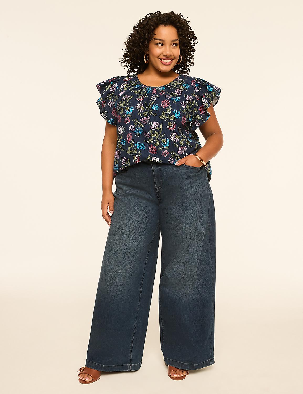 A smiling woman with curly hair stands in the foreground wearing a floral top and wide-leg jeans against a plain, light-colored background. Product Image 3