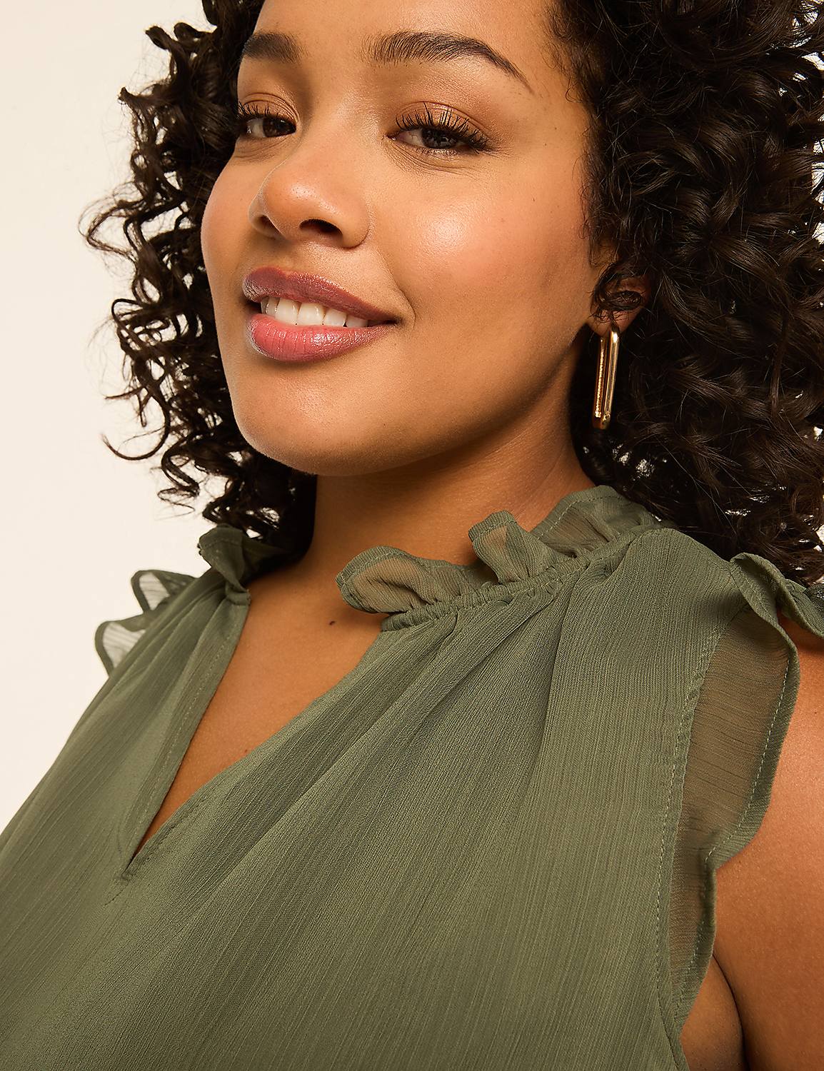 A woman with curly hair smiles at the camera, wearing a green ruffled top against a plain background. Product Image 4