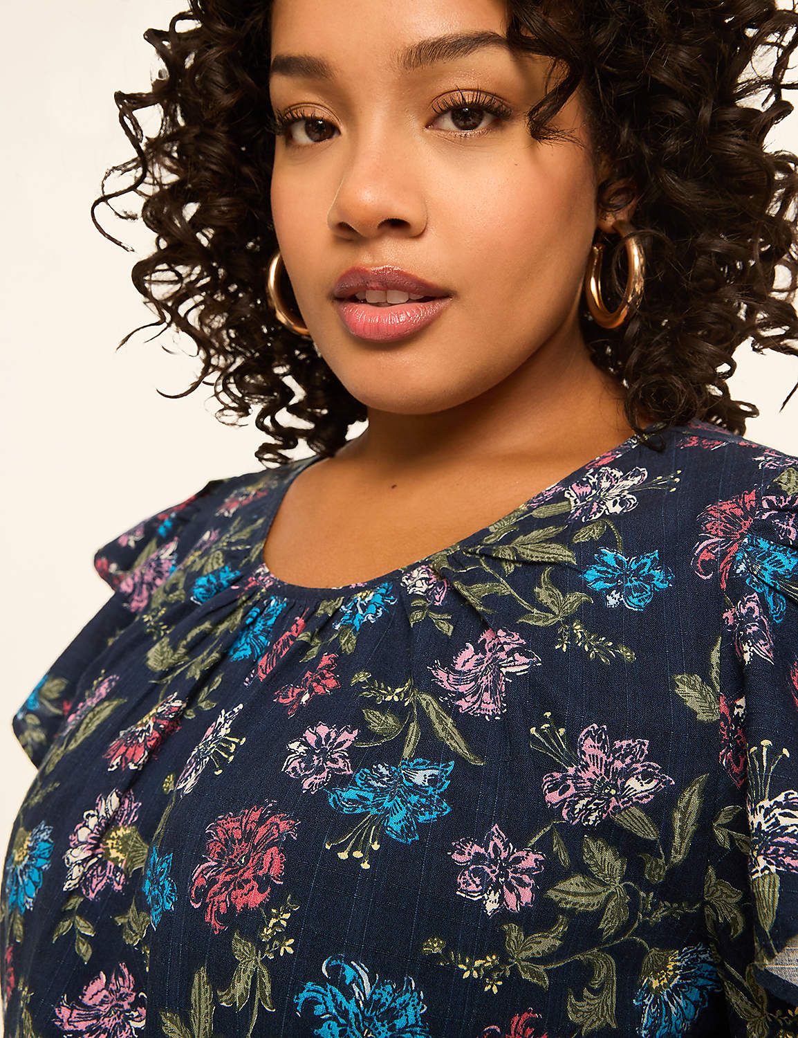 A woman with curly hair and gold hoop earrings smiles gently in the foreground, wearing a dark blue floral-print blouse against a plain, light background. Product Image 4