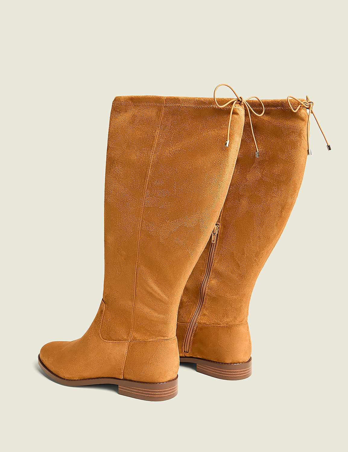 A pair of tan suede knee-high boots with tie details at the top are displayed against a plain, light beige background. Product Image 2