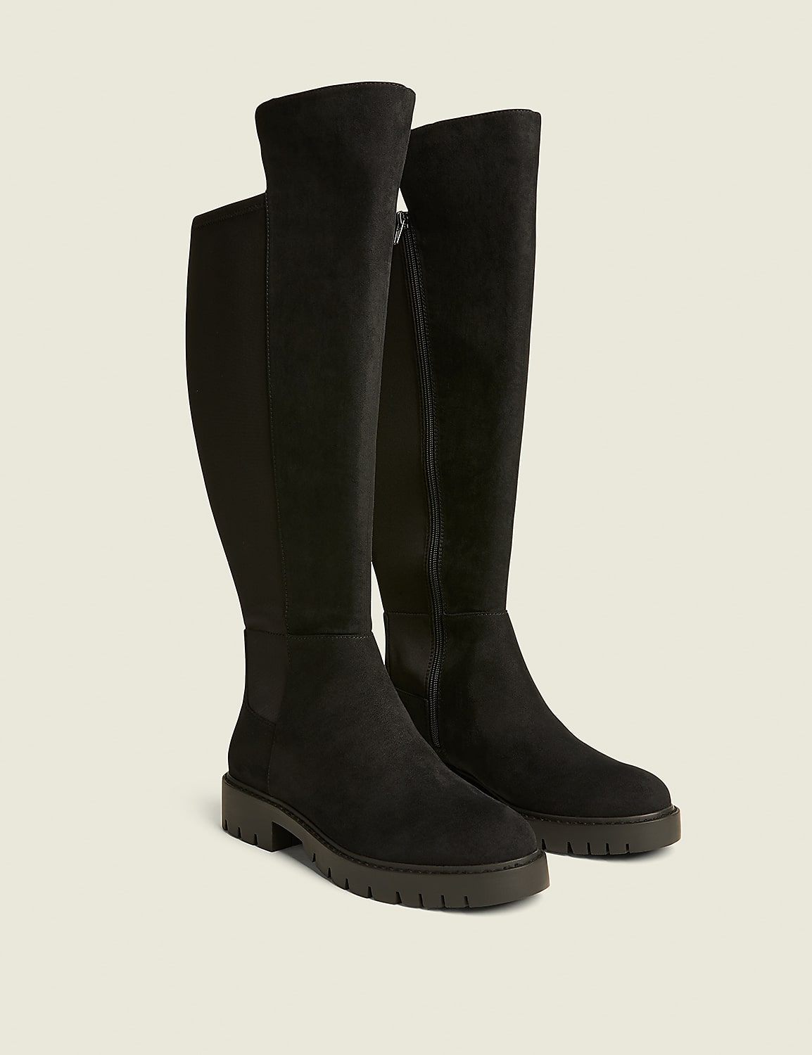A pair of black suede knee-high boots with a zipper and a thick sole stand on a light brown background. Product Image 1