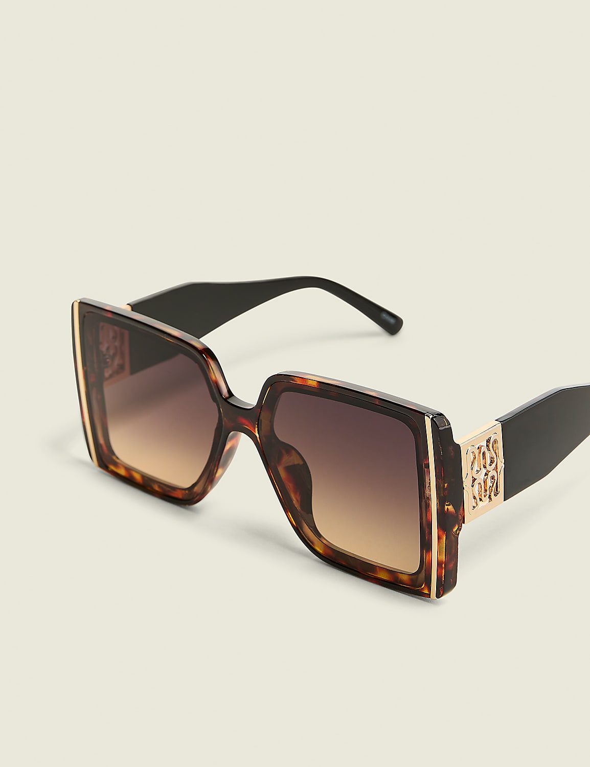 Oversized tortoiseshell sunglasses with gold accents rest on a plain, light-colored background. Product Image 1
