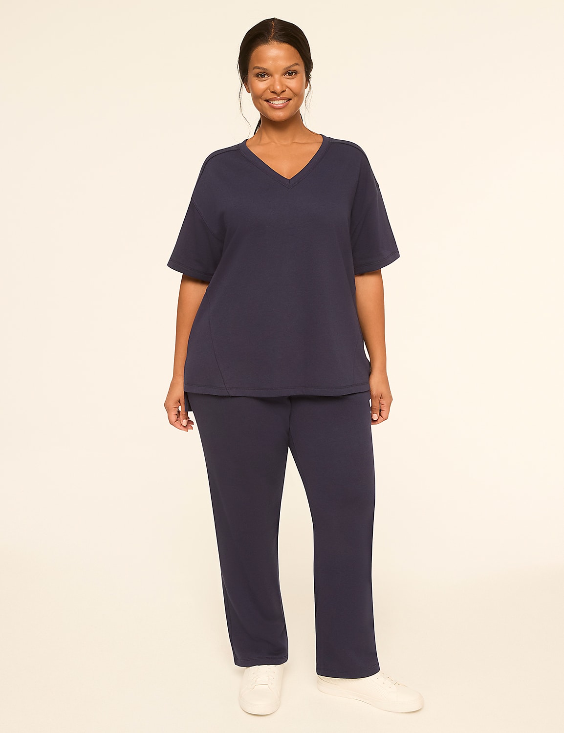 A smiling woman in a navy blue v-neck t-shirt and matching pants stands against a plain, light-colored background. Product Image 3