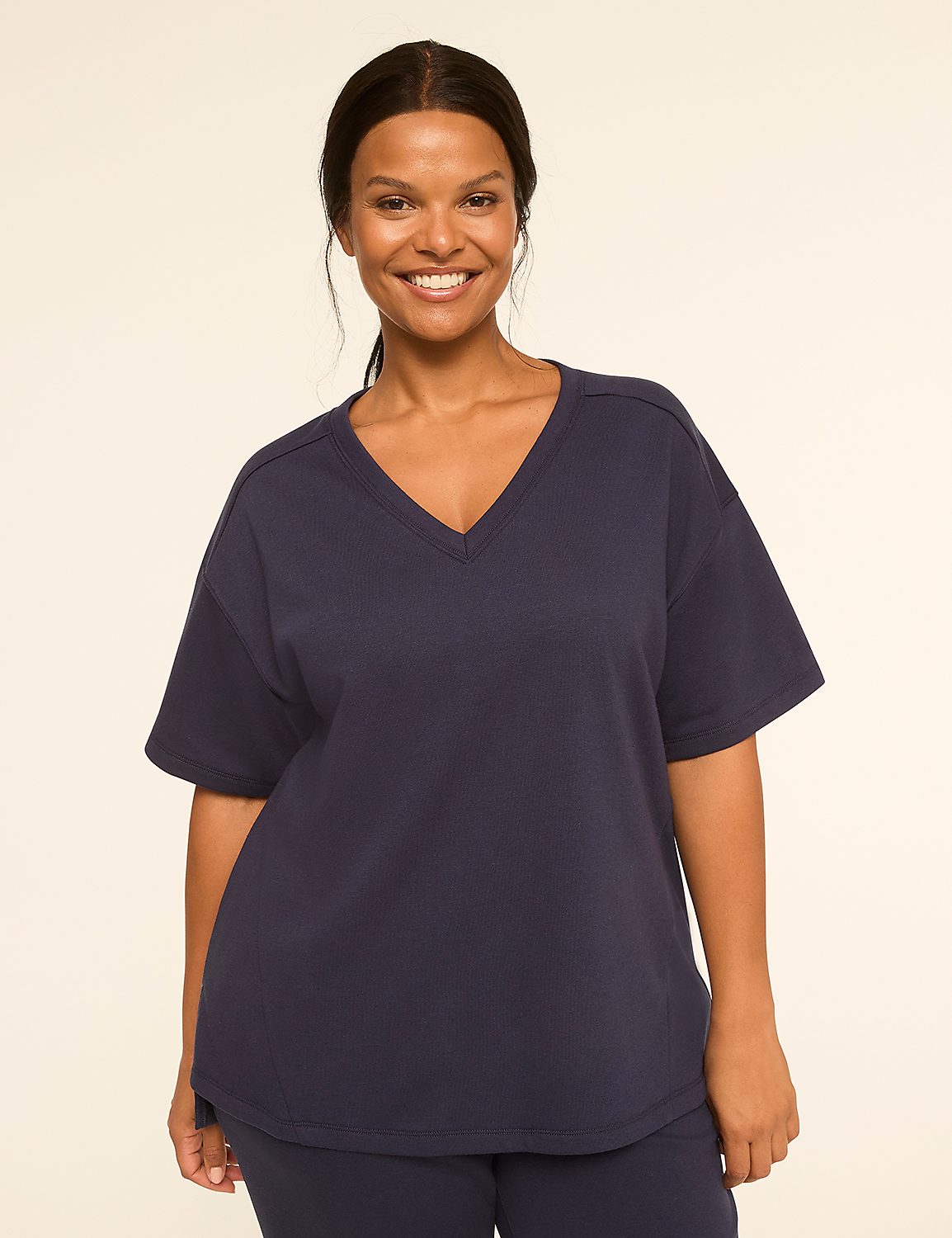 A smiling woman in a navy blue v-neck t-shirt stands against a plain, light background. Product Image 1