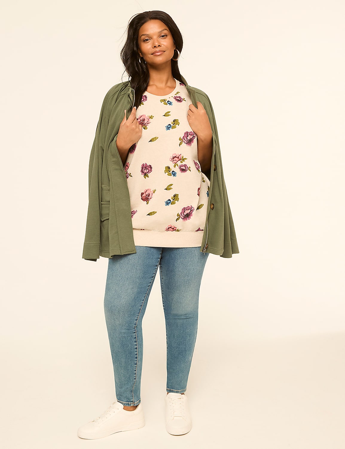 A woman in a floral sweatshirt and jeans stands against a plain, light background, with a green jacket draped over her shoulders. Product Image 3