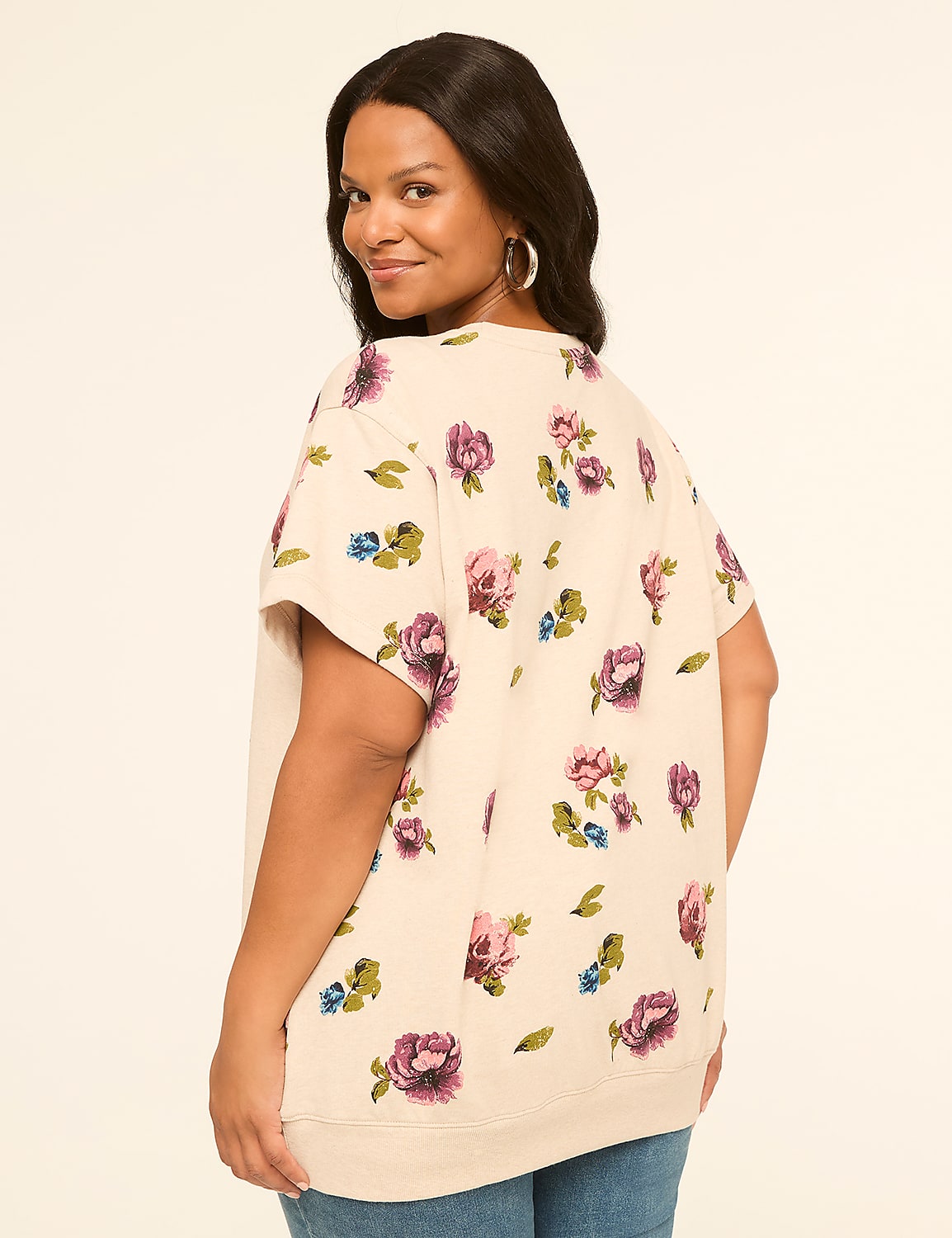 A woman in a floral print top and jeans smiles over her shoulder against a plain, light background. Product Image 2