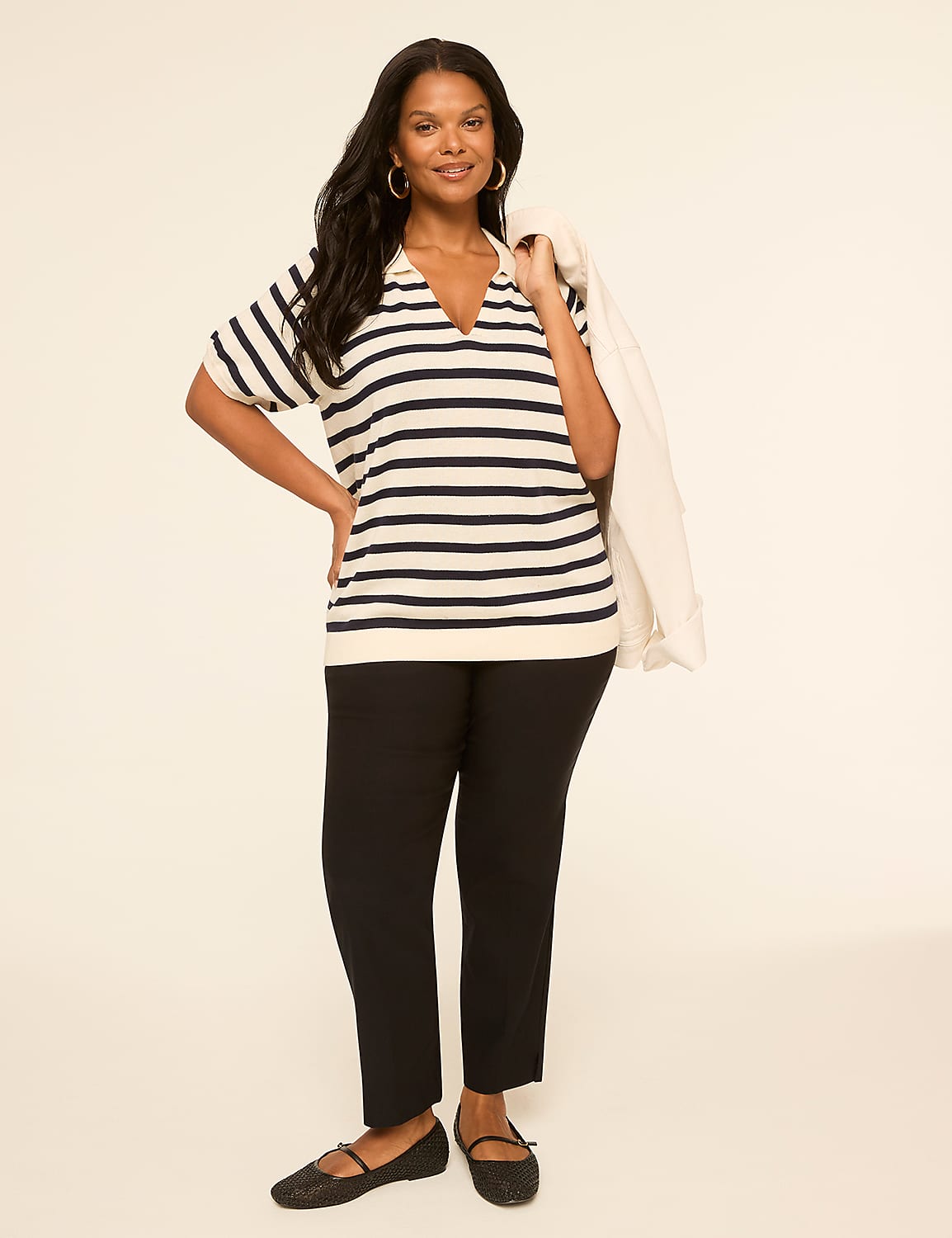A woman in a striped shirt and black pants stands against a plain, light-colored background, with a white jacket draped over her shoulder. Product Image 3