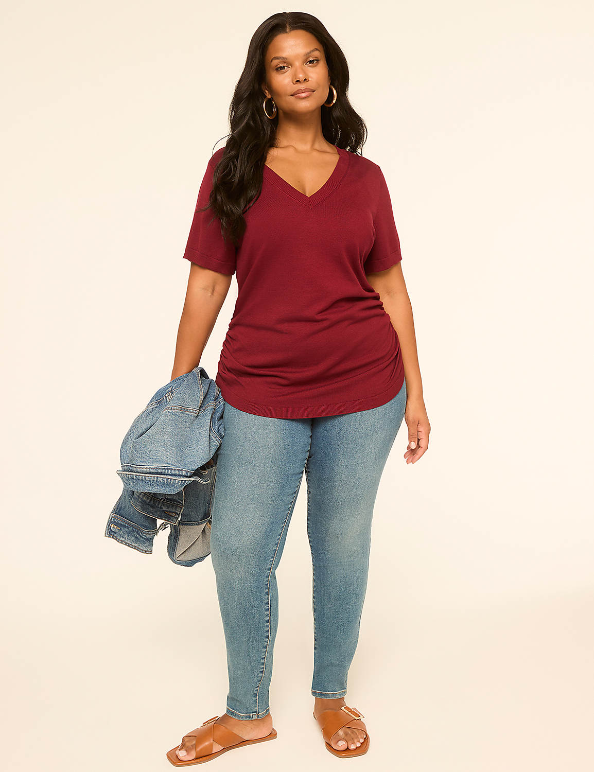 A woman in a maroon v-neck shirt and jeans stands against a plain, light-colored background, holding a denim jacket. Product Image 3