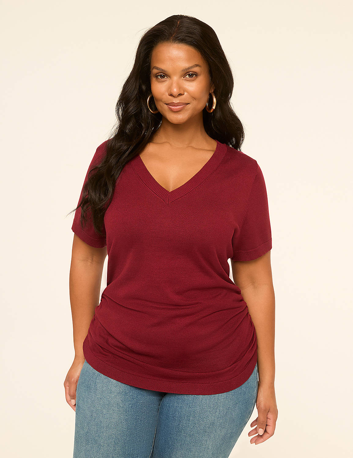 A woman in a maroon v-neck shirt and blue jeans stands against a plain, light-colored background. Product Image 1