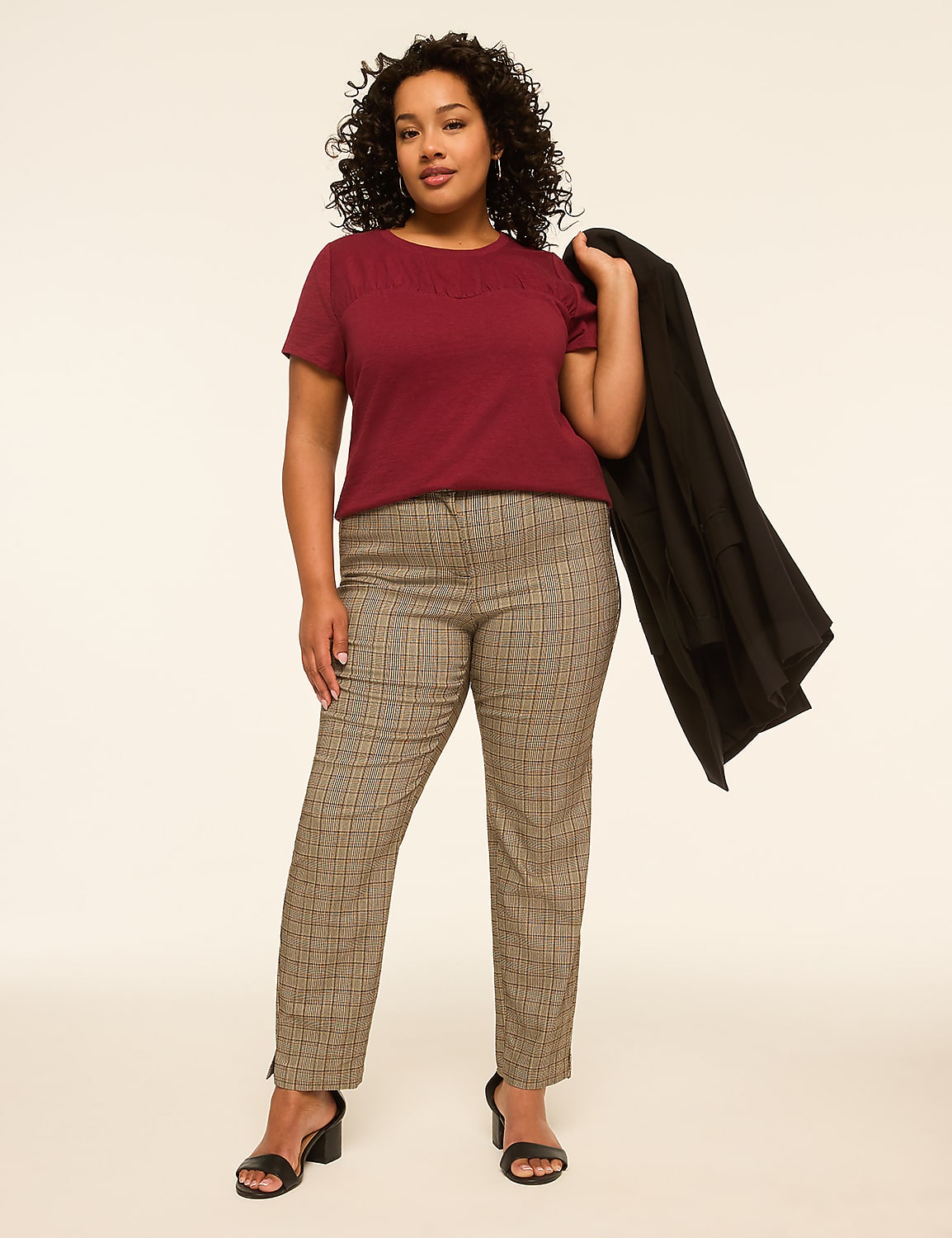 A woman in a maroon top and plaid pants stands against a plain, light background, holding a black jacket over her shoulder. Product Image 3