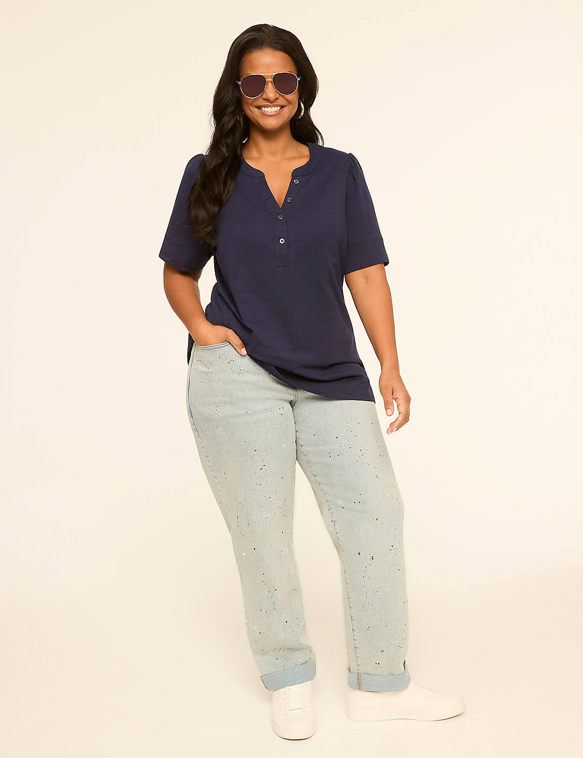 A smiling woman in a navy blue top and light-wash jeans stands against a plain, light-colored background. Product Image 3