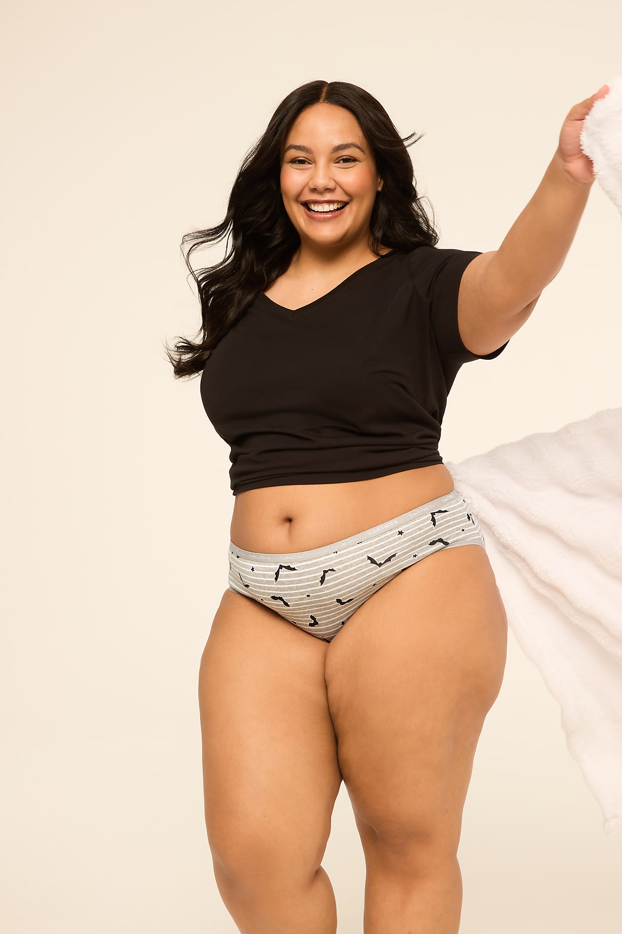 A smiling woman in a black t-shirt and patterned underwear poses against a plain, light background, holding a white cloth. Product Image 4