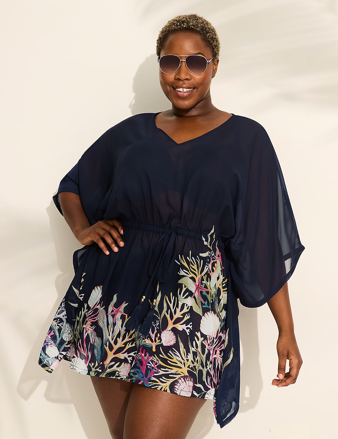 A woman in a navy blue cover-up with a coral print stands against a white background with palm leaf shadows. Product Image 1