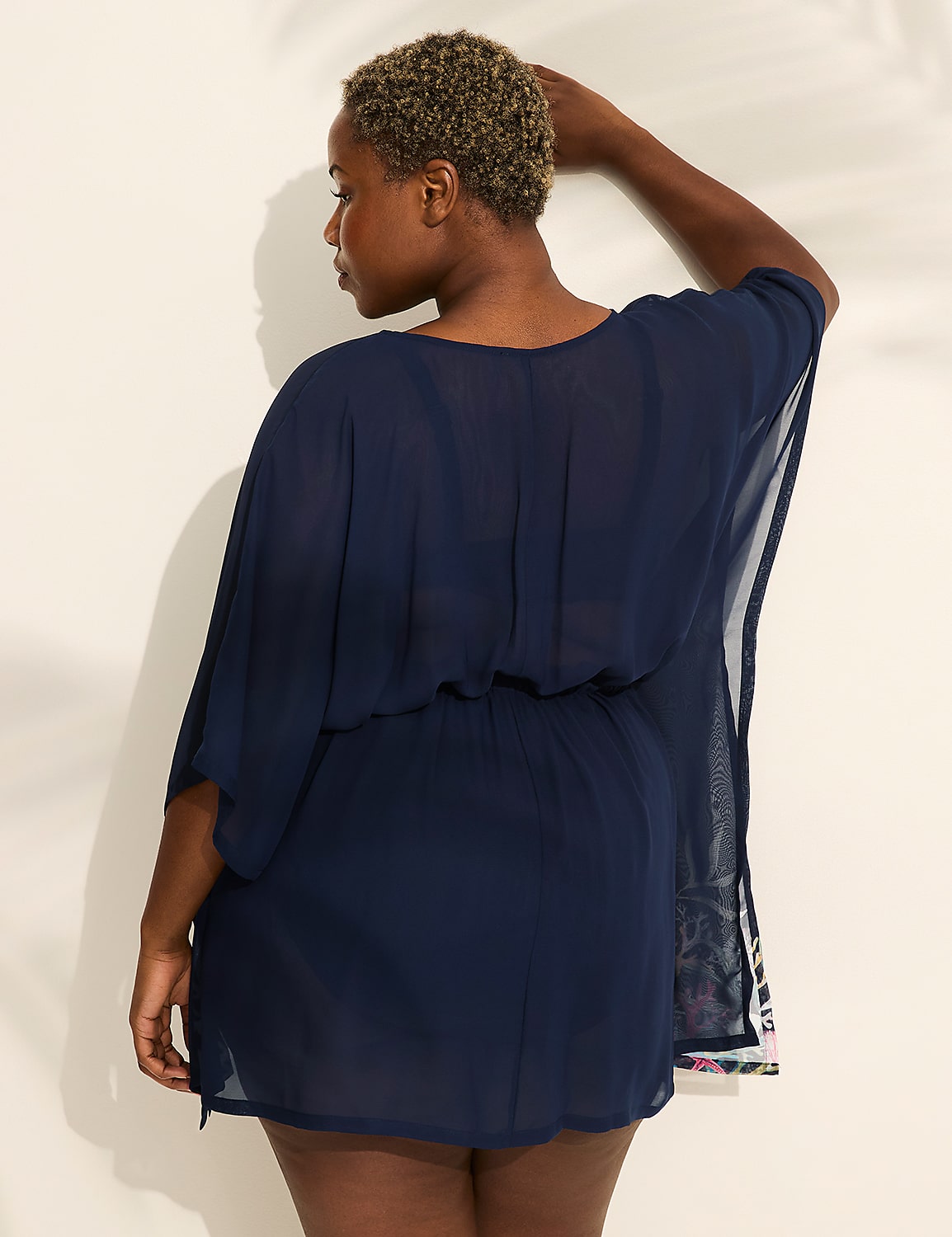 A woman in a navy blue sheer cover-up stands against a white wall with palm leaf shadows. Product Image 2