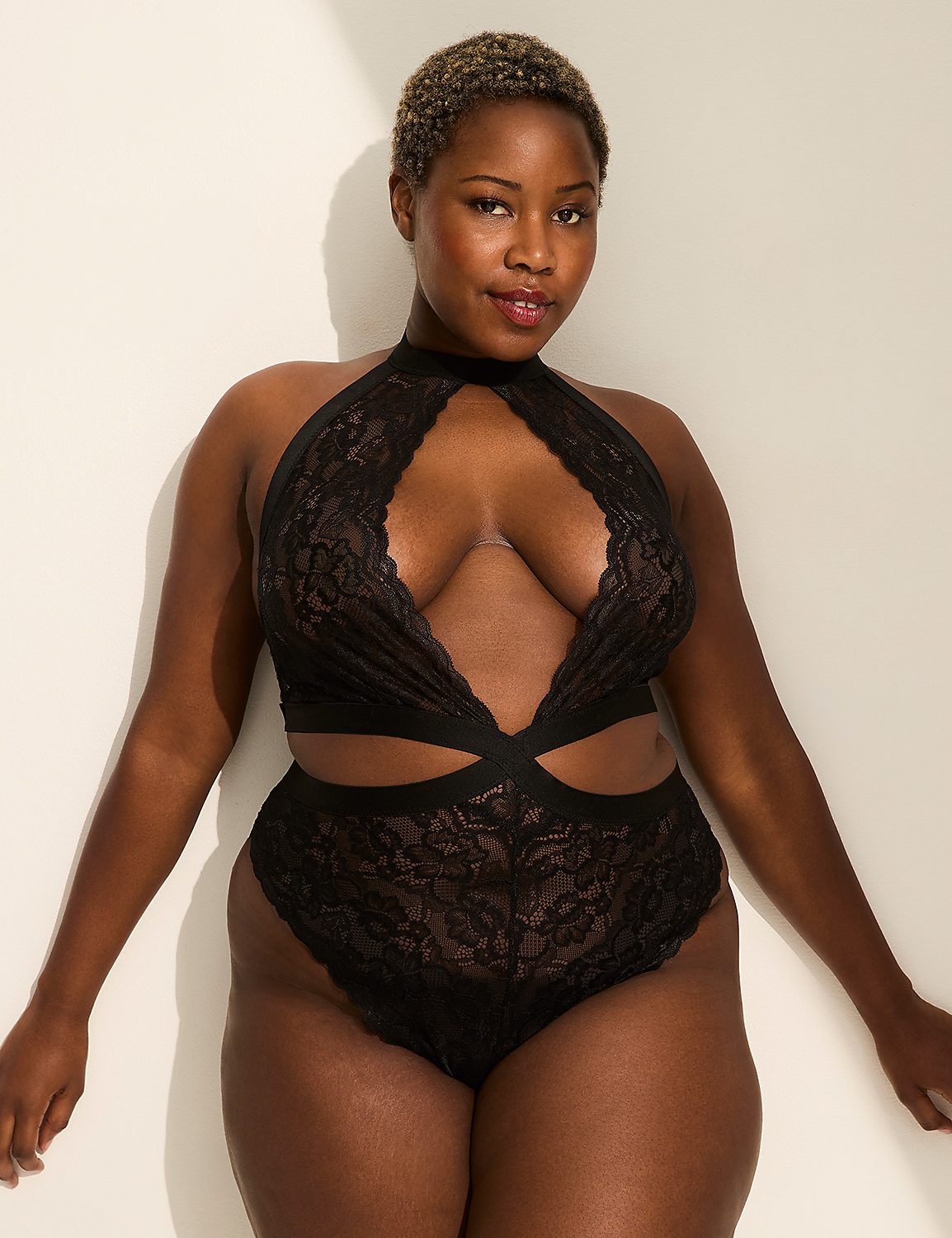 A woman in a black lace bodysuit poses against a plain white wall with soft lighting. Product Image 1