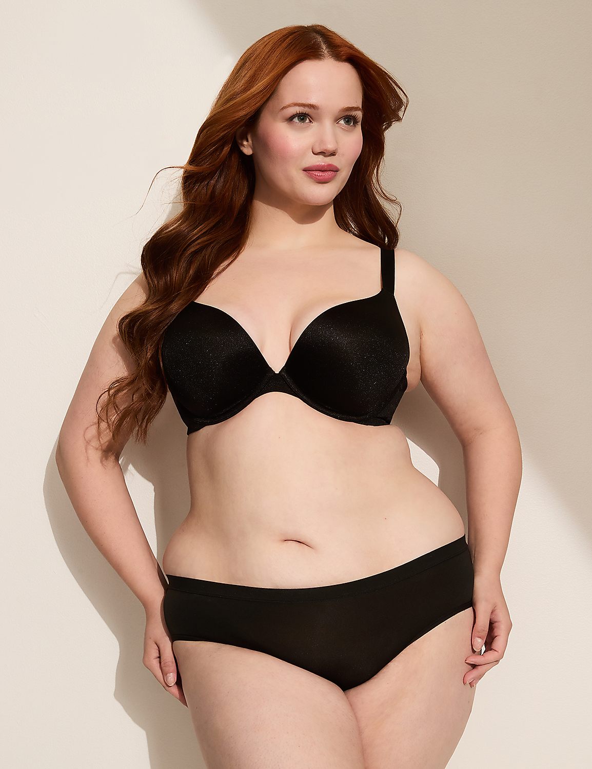 A woman with red hair poses in black lingerie against a plain, light-colored background with a shadow cast from the left. Product Image 5