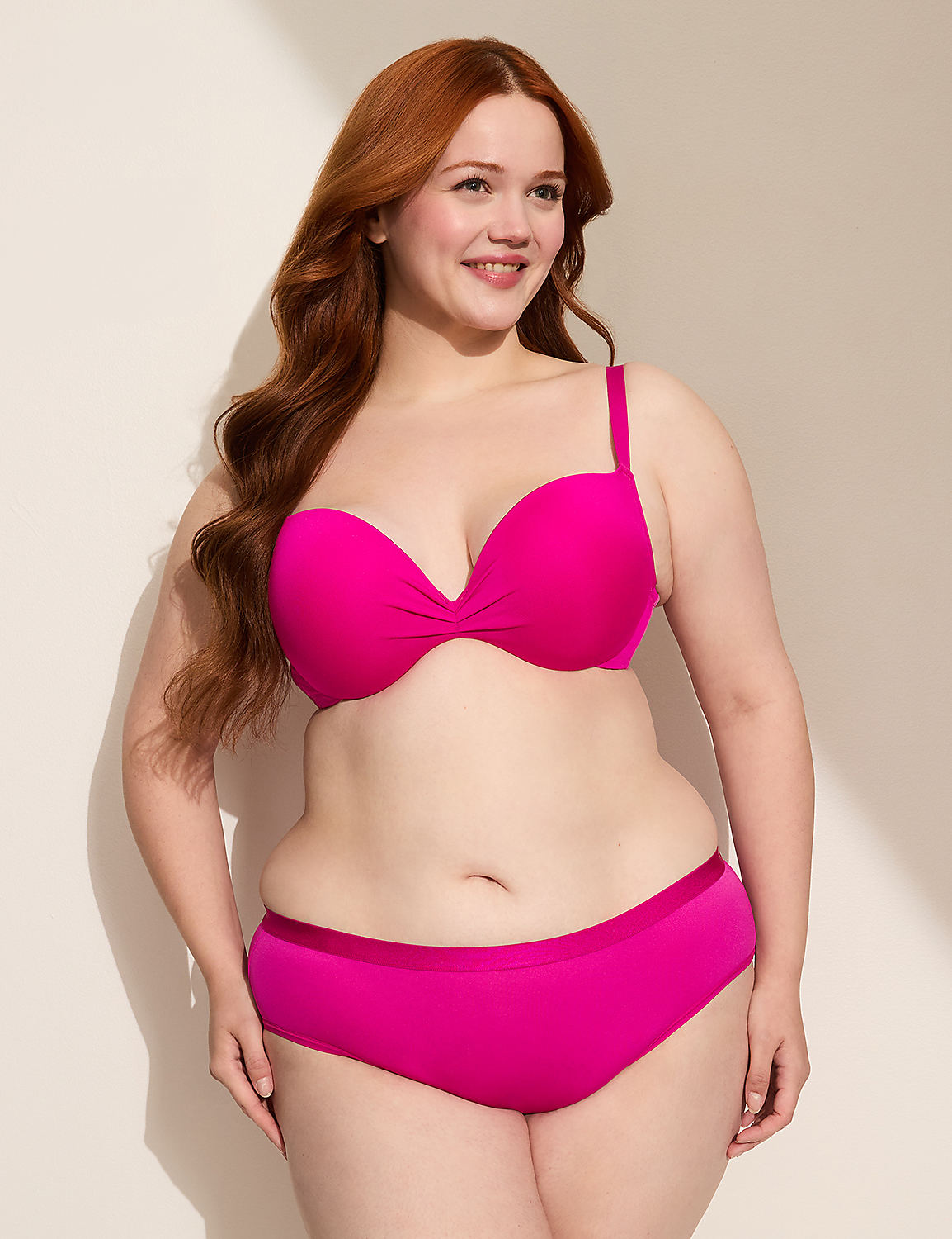 A smiling woman with long red hair poses in a bright pink bikini against a plain, light-colored wall with soft shadows. Product Image 3