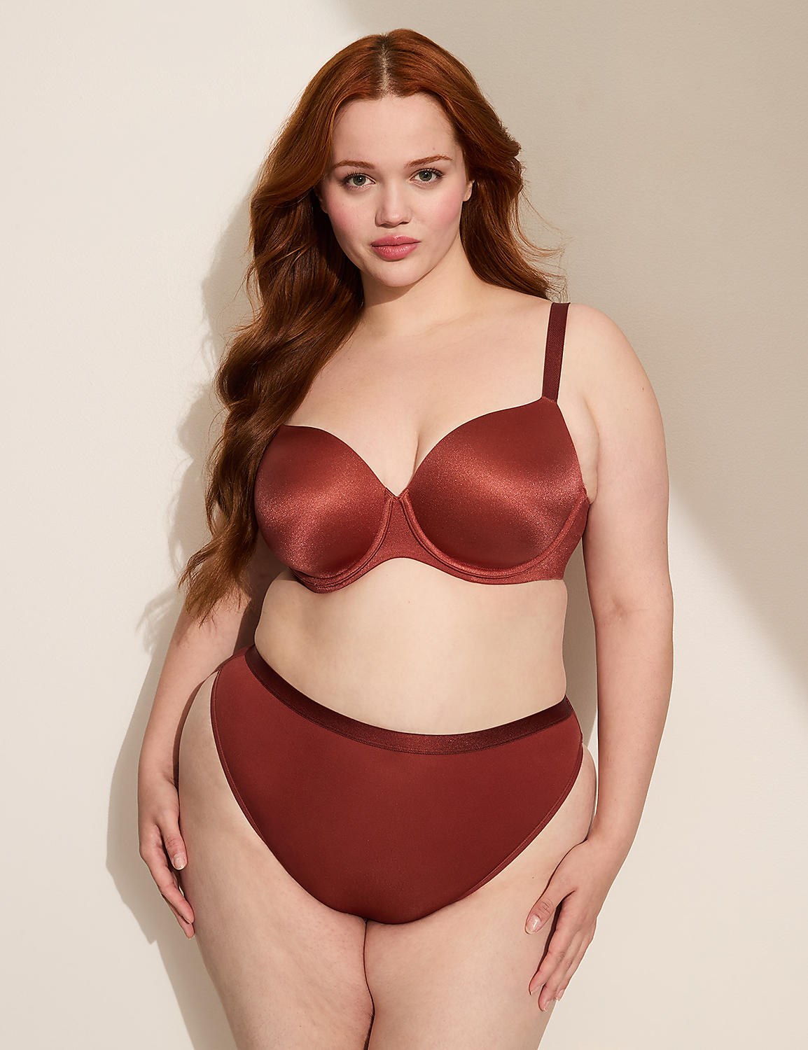 A woman with long, wavy red hair poses in a rust-colored bra and matching high-waisted underwear against a plain, light-colored wall with a subtle shadow. Product Image 4