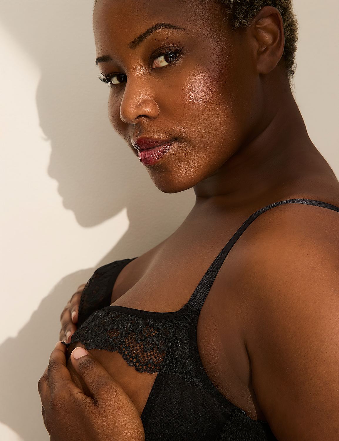 A woman in a black lace-trimmed bra holds her hand to her chest against a wall with a shadow. Product Image 2