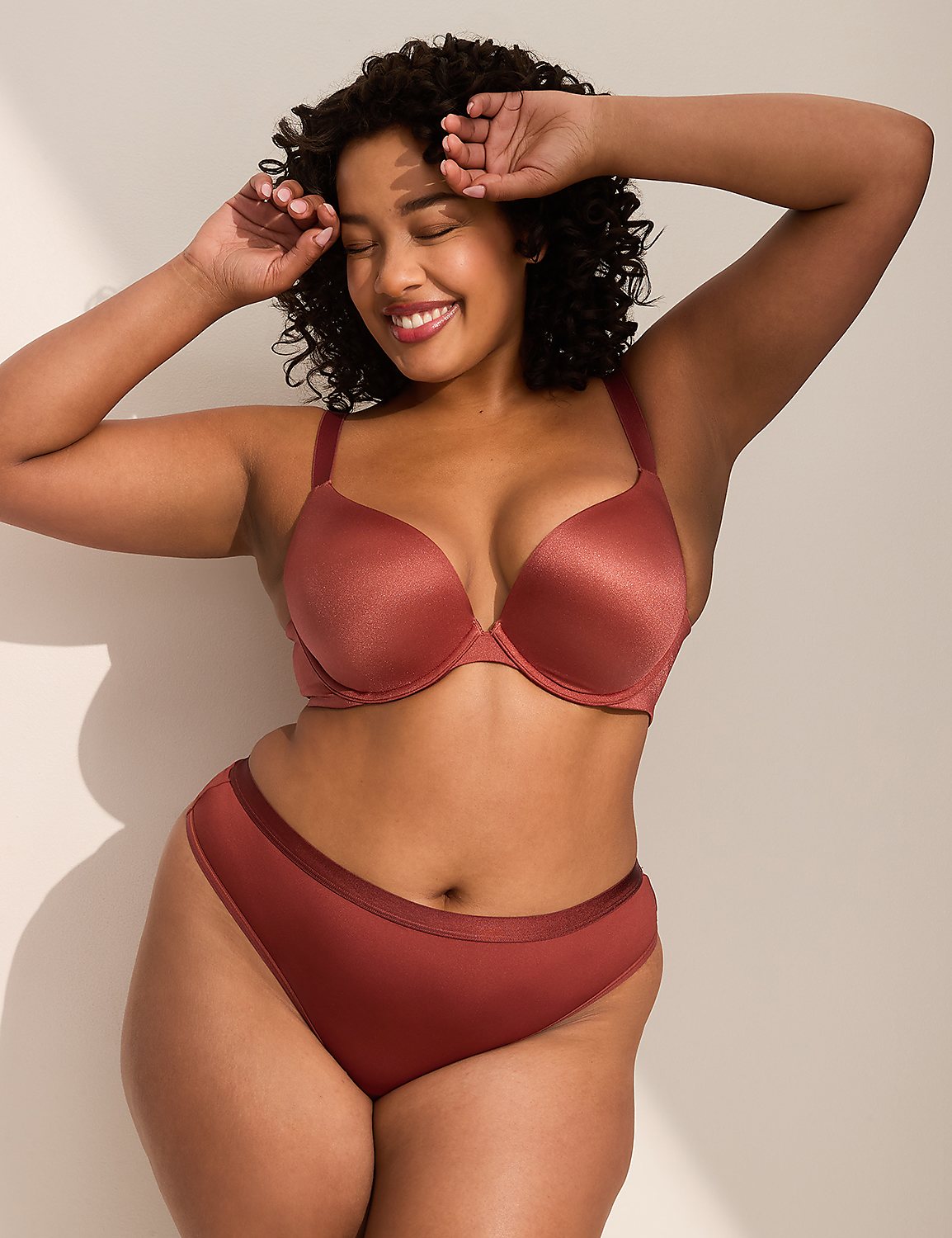 A woman in a rust-colored bra and underwear smiles with her eyes closed and hands behind her head, against a plain background with soft shadows. Product Image 4