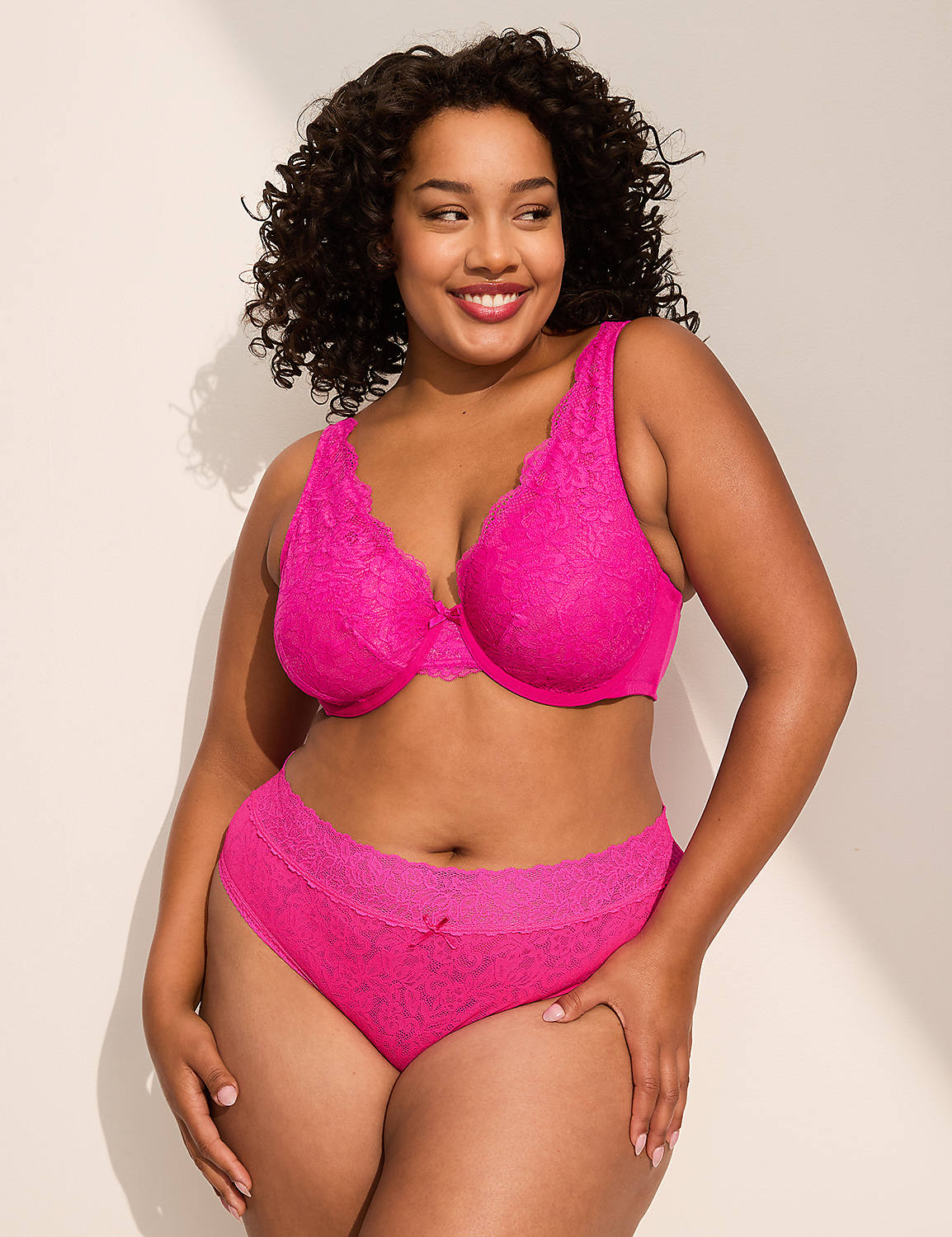 A smiling woman in a bright pink lace bra and matching underwear stands against a plain, softly lit background. Product Image 3