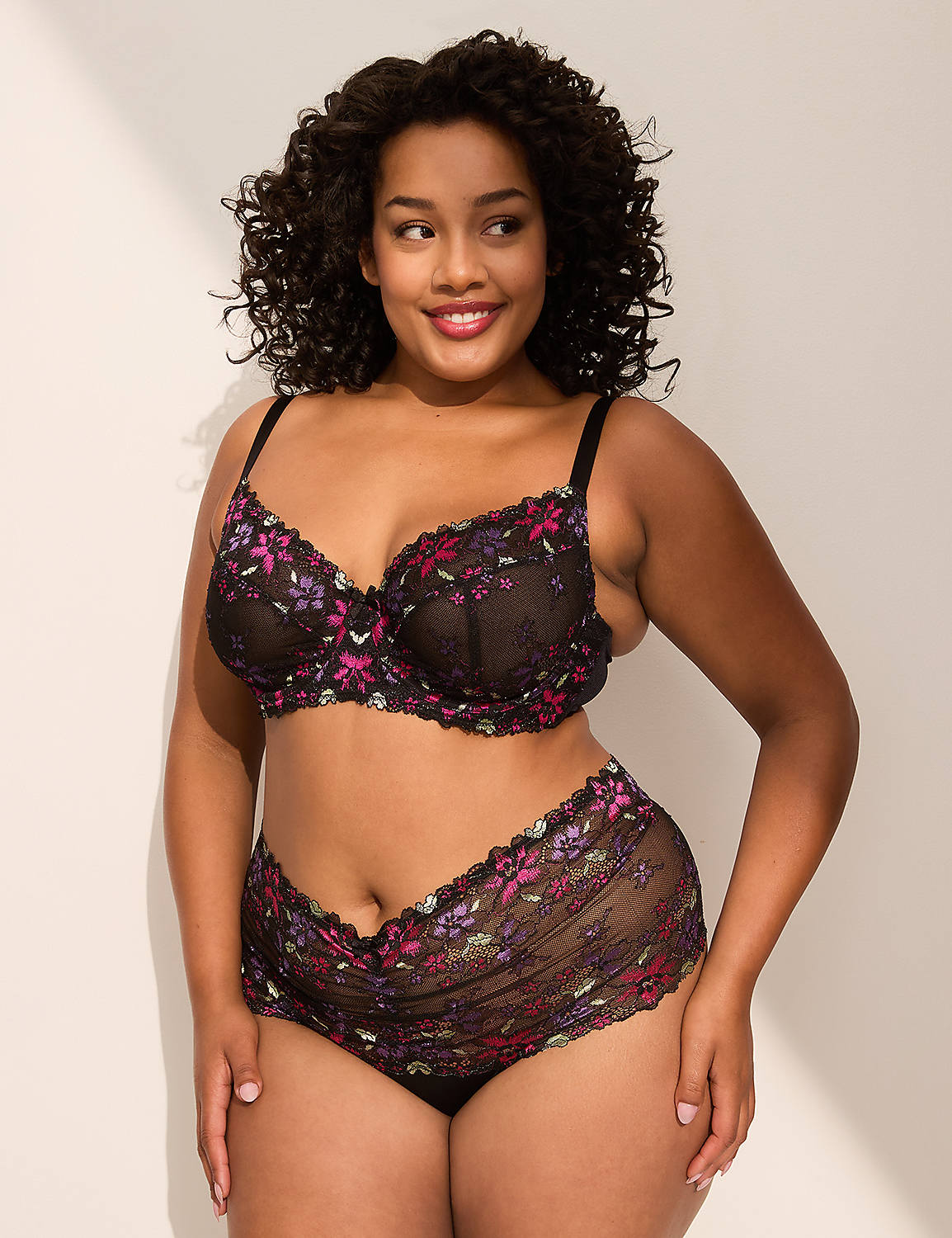 A smiling woman in floral lingerie stands against a plain, light-colored wall with shadows. Product Image 4