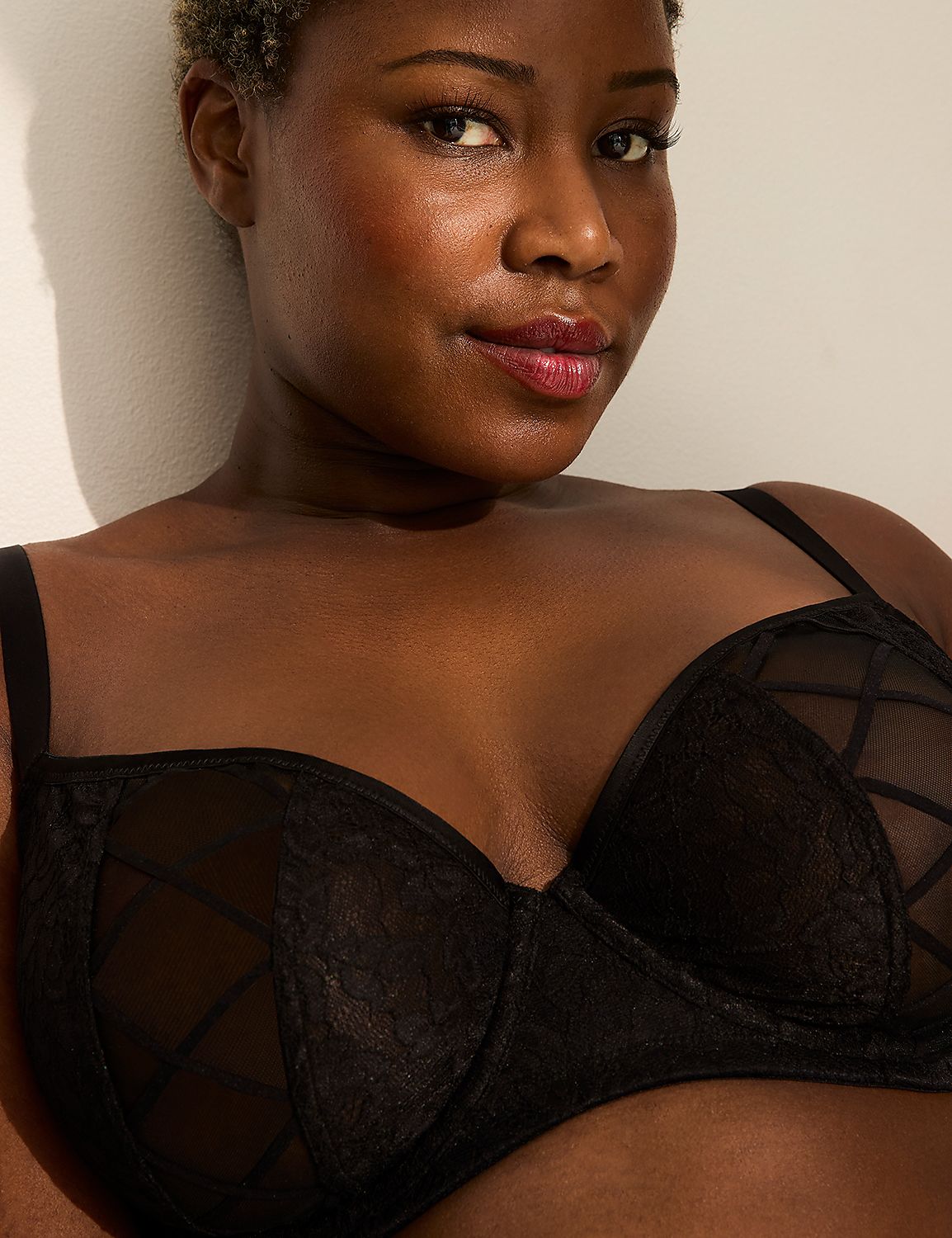 A woman with dark skin and short, curly hair poses in a black lace bra against a plain white wall. Product Image 2