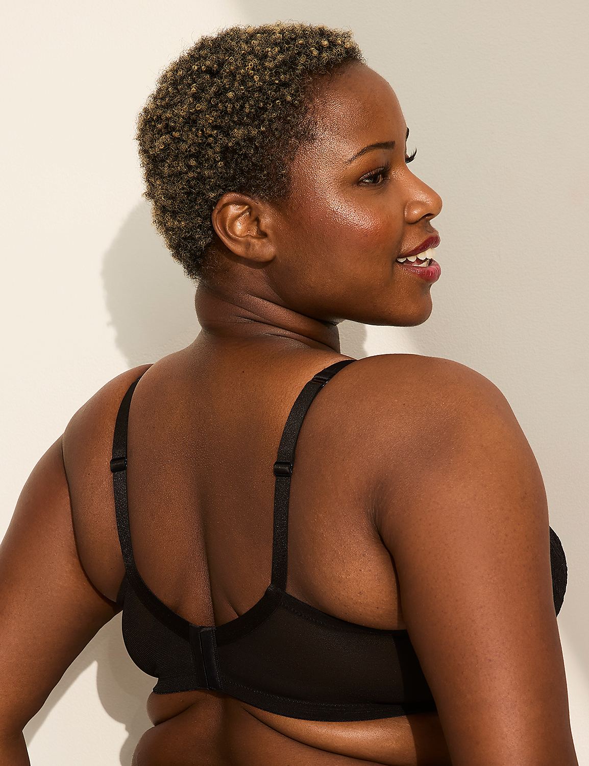 A woman in a black bra smiles as she looks to the side against a plain, light-colored background. Product Image 3