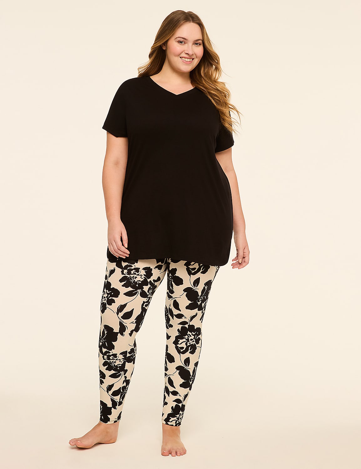 A smiling woman in a black v-neck shirt and floral leggings stands against a plain, light-colored background. Product Image 1