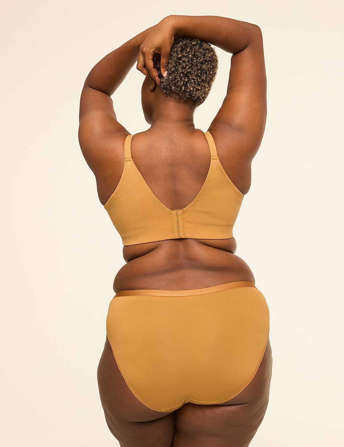 A woman with dark skin and curly hair stands with her back to the viewer, arms raised behind her head, wearing a tan bra and matching underwear against a plain, light background. Product Image 2