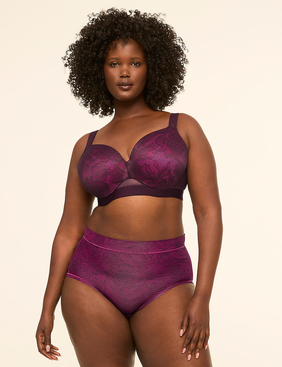 A woman with dark curly hair poses in a purple lace bra and matching high-waisted underwear against a plain cream background. Product Image 4