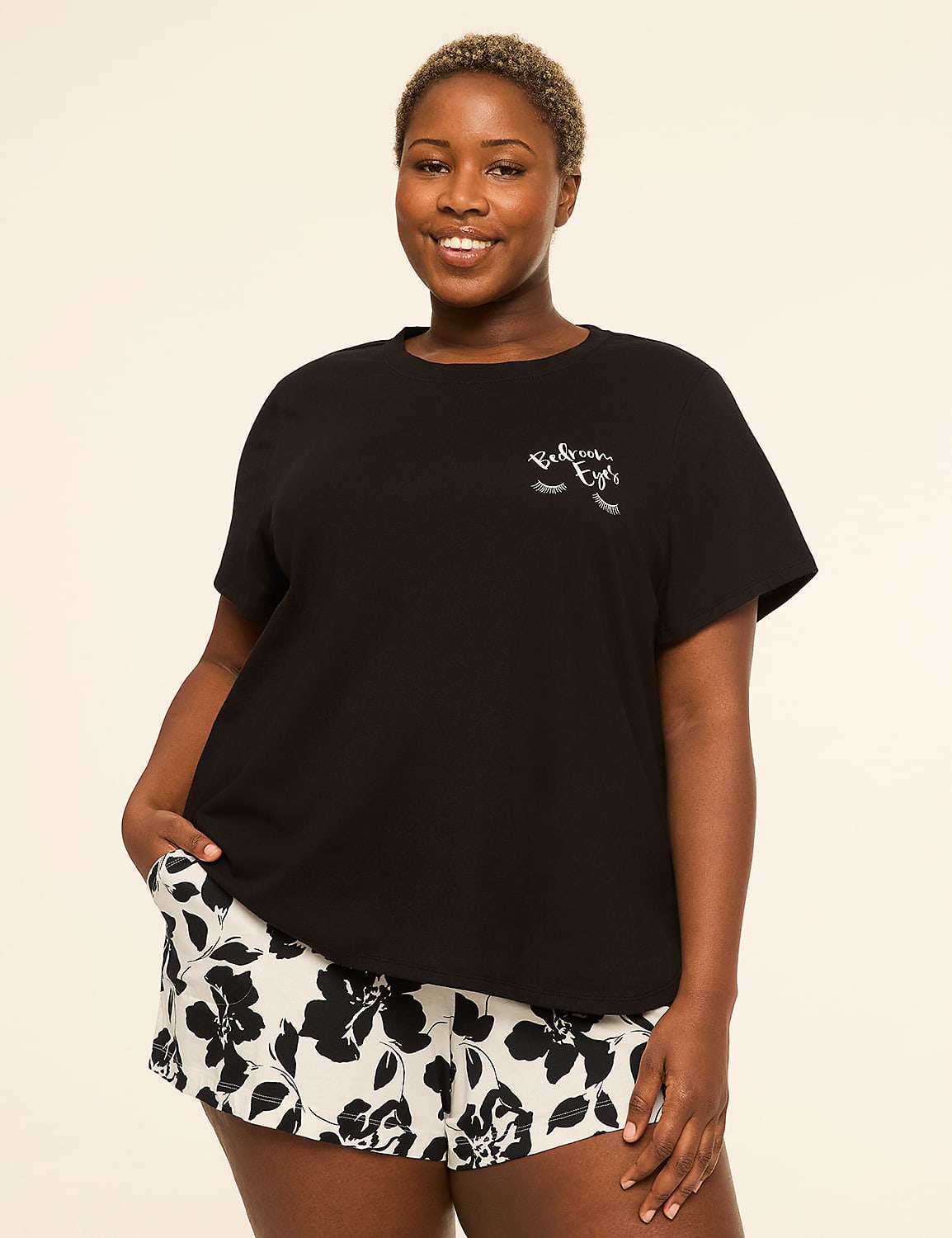 A smiling woman in a black t-shirt and floral shorts stands against a plain, light-colored background. Product Image 1
