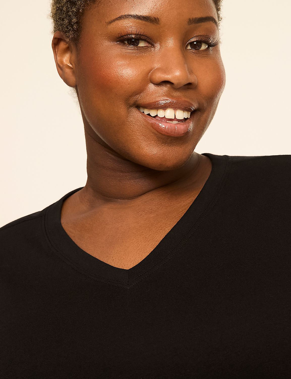 A smiling woman with short, curly hair wears a black V-neck shirt against a plain, light background. Product Image 4