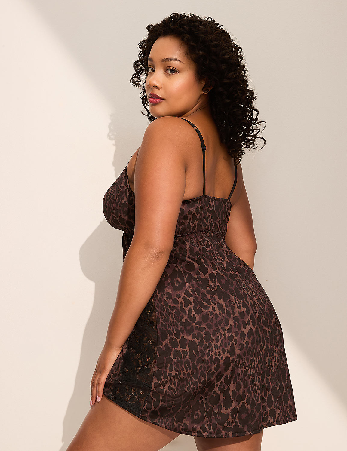 A woman in a leopard-print slip dress poses against a plain, light-colored wall with a shadow cast from the side. Product Image 2