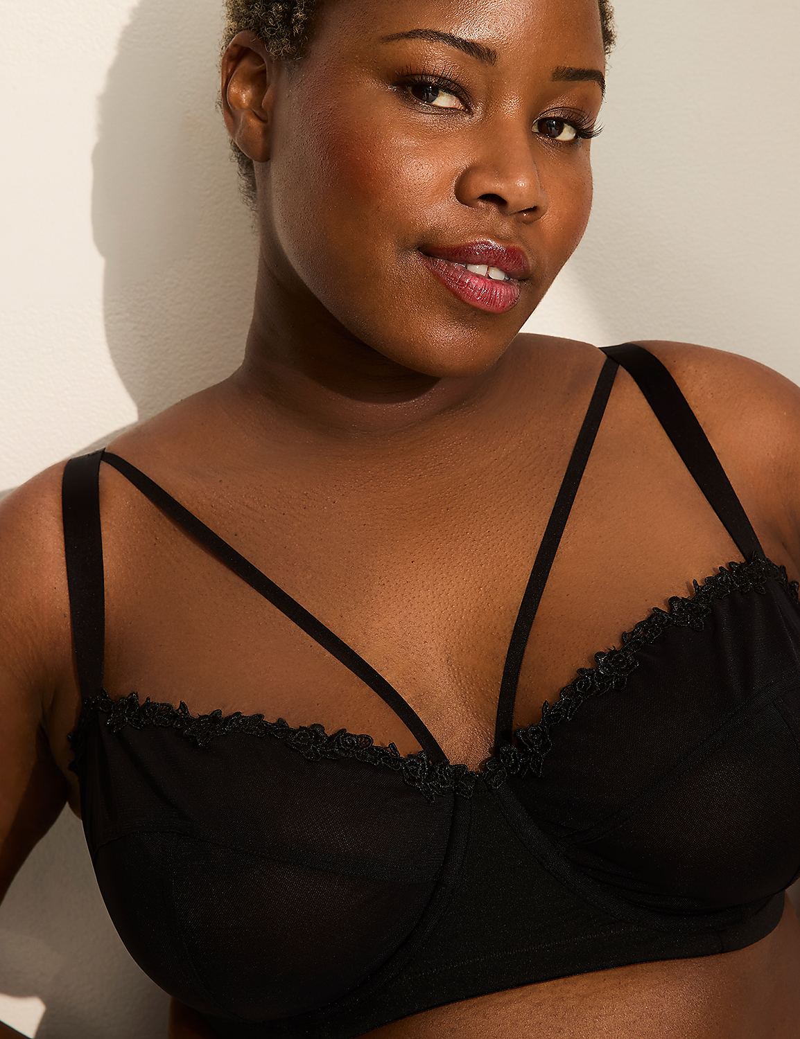 A woman with dark skin and short hair wears a black bra with delicate straps, set against a plain, light-colored wall. Product Image 2