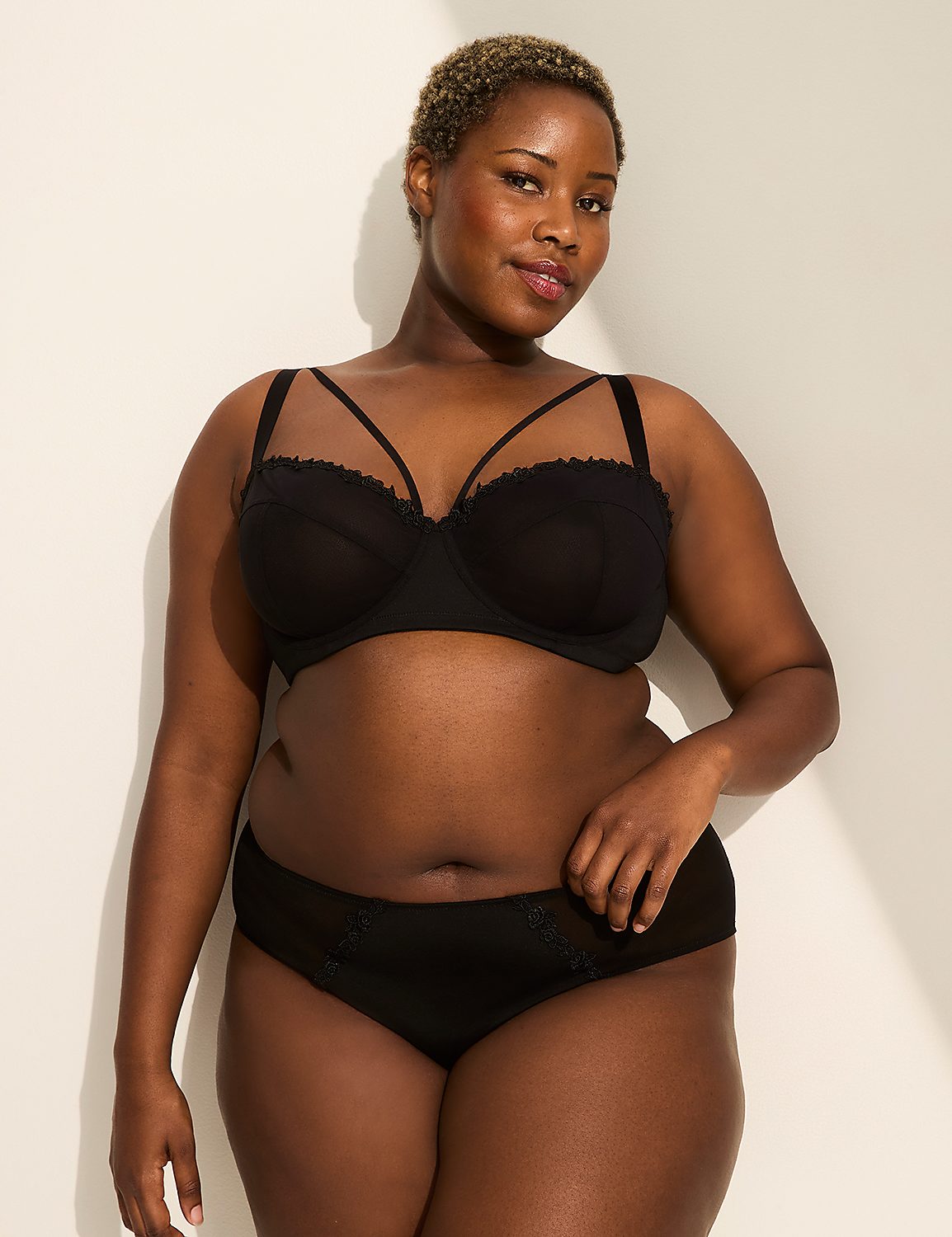 A plus-size Black woman in a black bra and underwear stands against a plain, light-colored wall with a shadow cast on it. Product Image 4