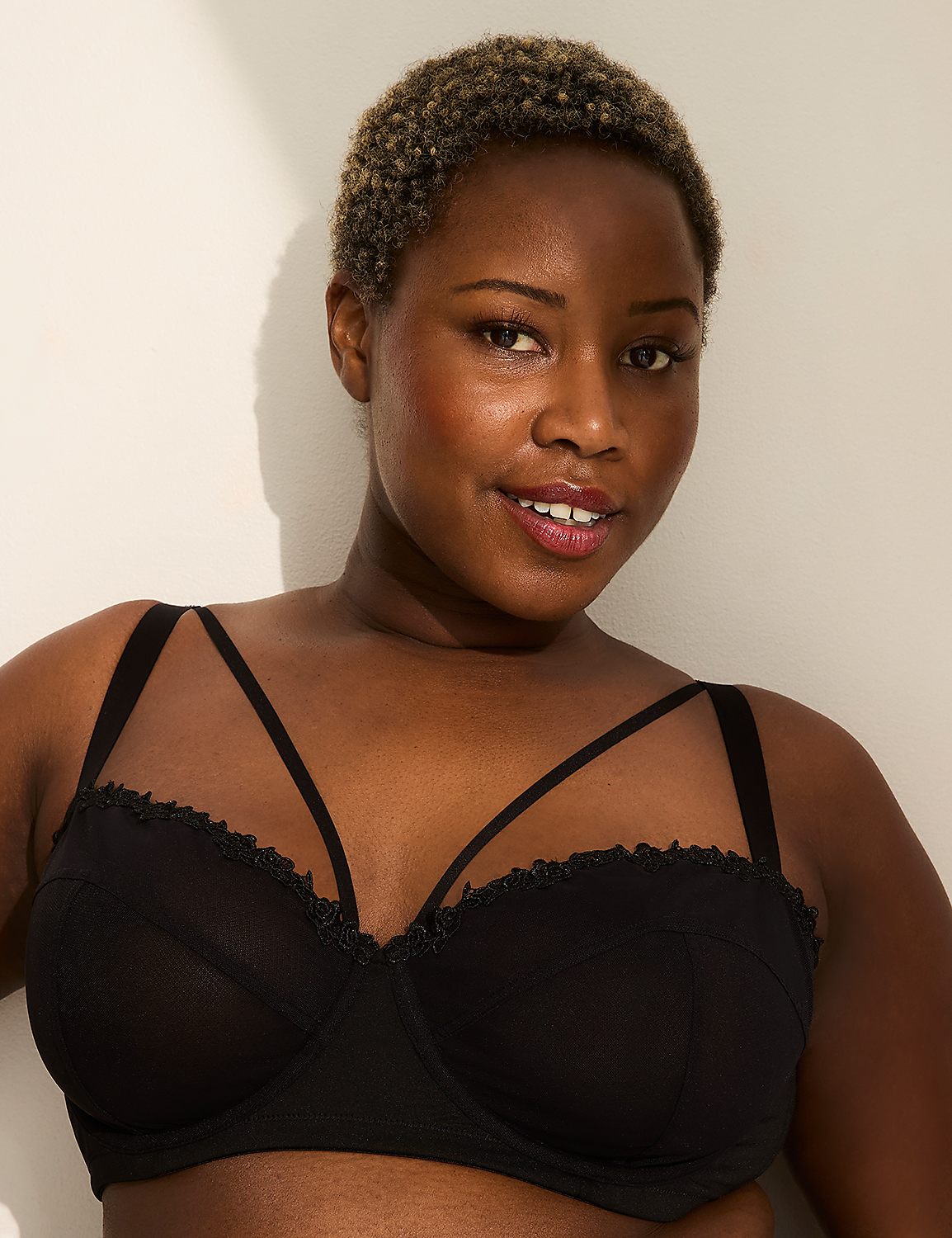 A woman with short, curly hair smiles at the camera, wearing a black bra with strappy detailing, against a plain white background. Product Image 1
